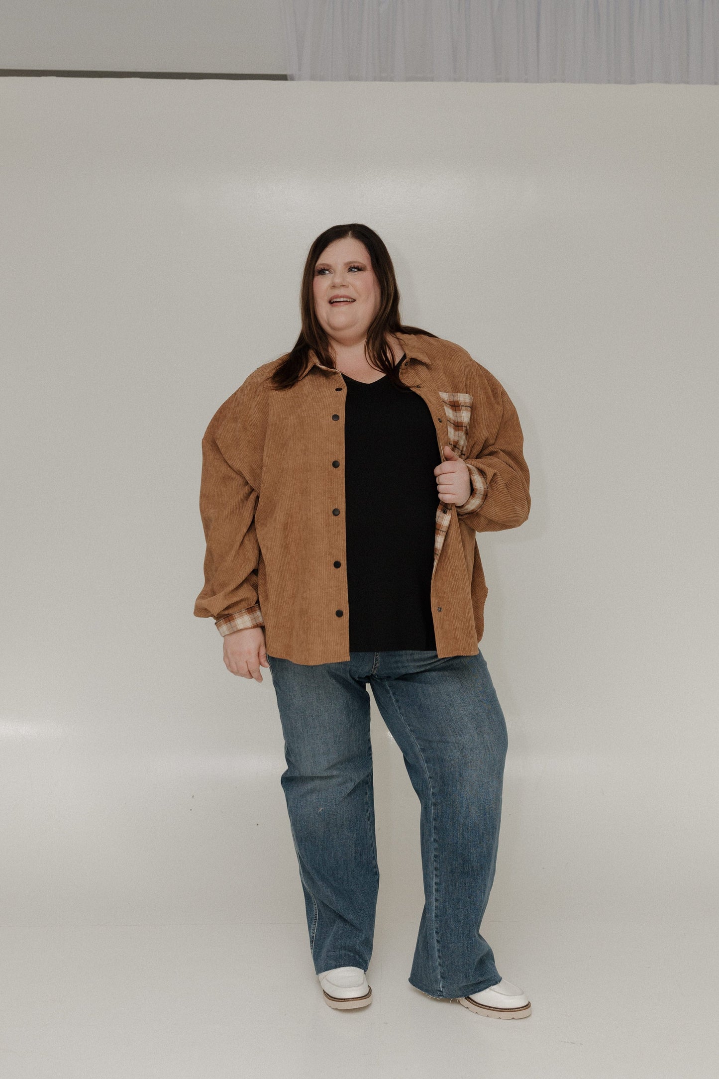 Person wearing a brown jacket, black shirt, and blue jeans on a white background