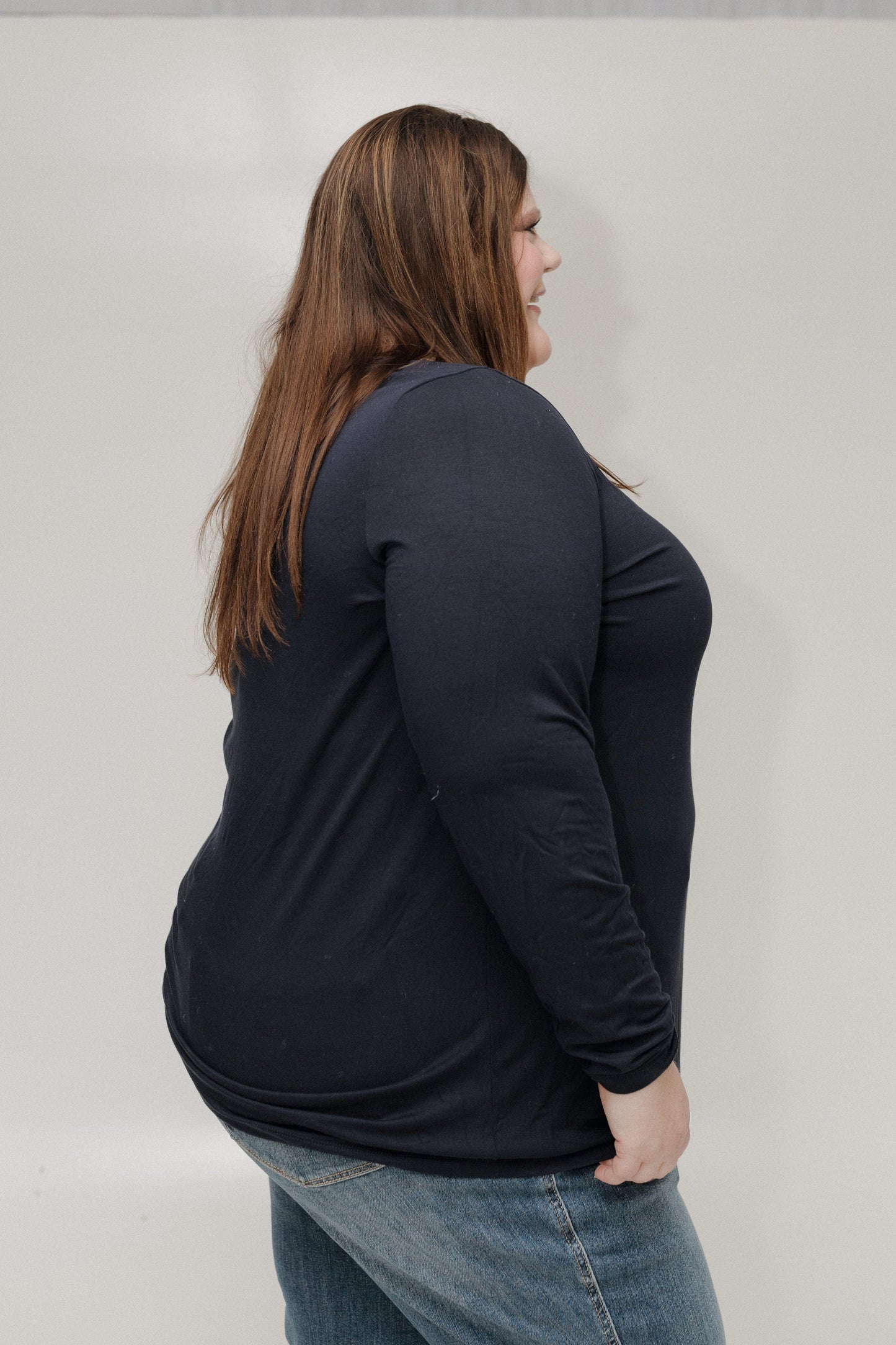 Person wearing a black long-sleeve shirt and blue jeans against a plain background