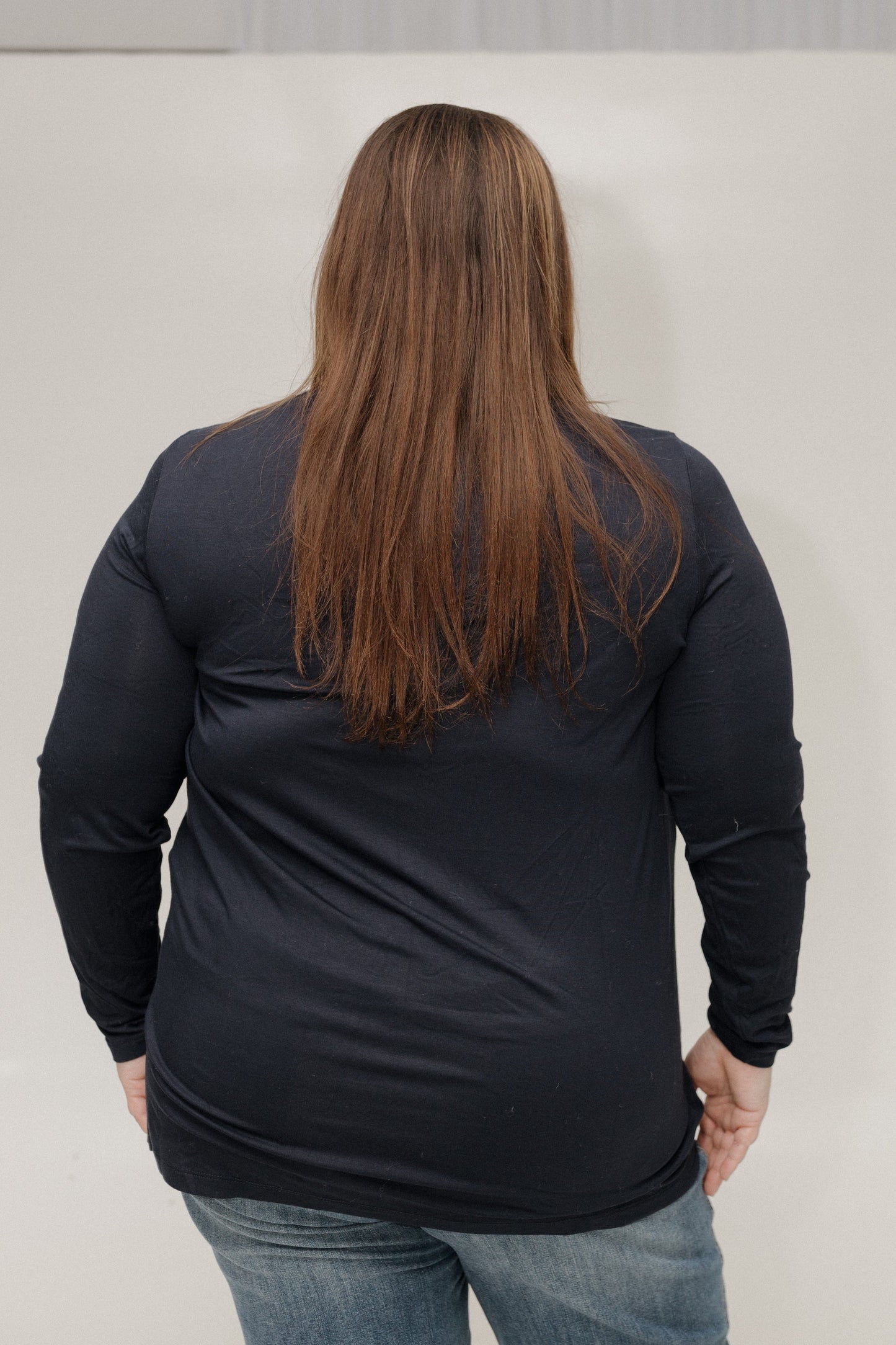 Person wearing a black long-sleeve shirt and blue jeans against a plain background