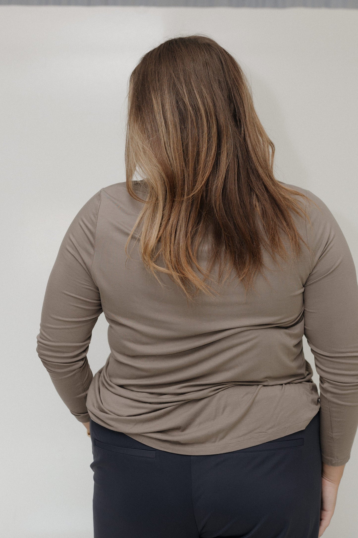 Person wearing a beige long-sleeve top and dark pants against a plain background