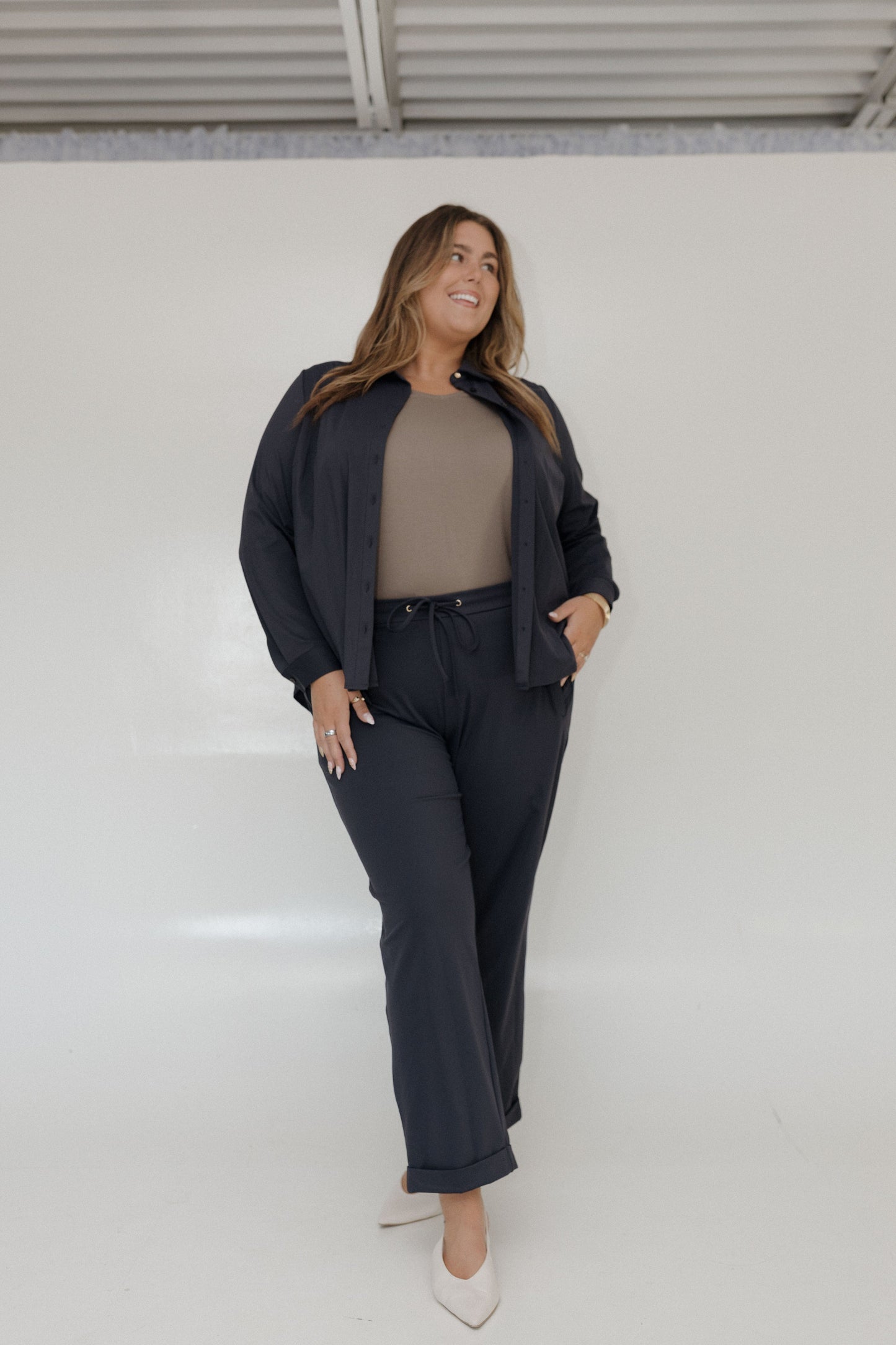 Woman wearing a black outfit with a beige top against a white wall