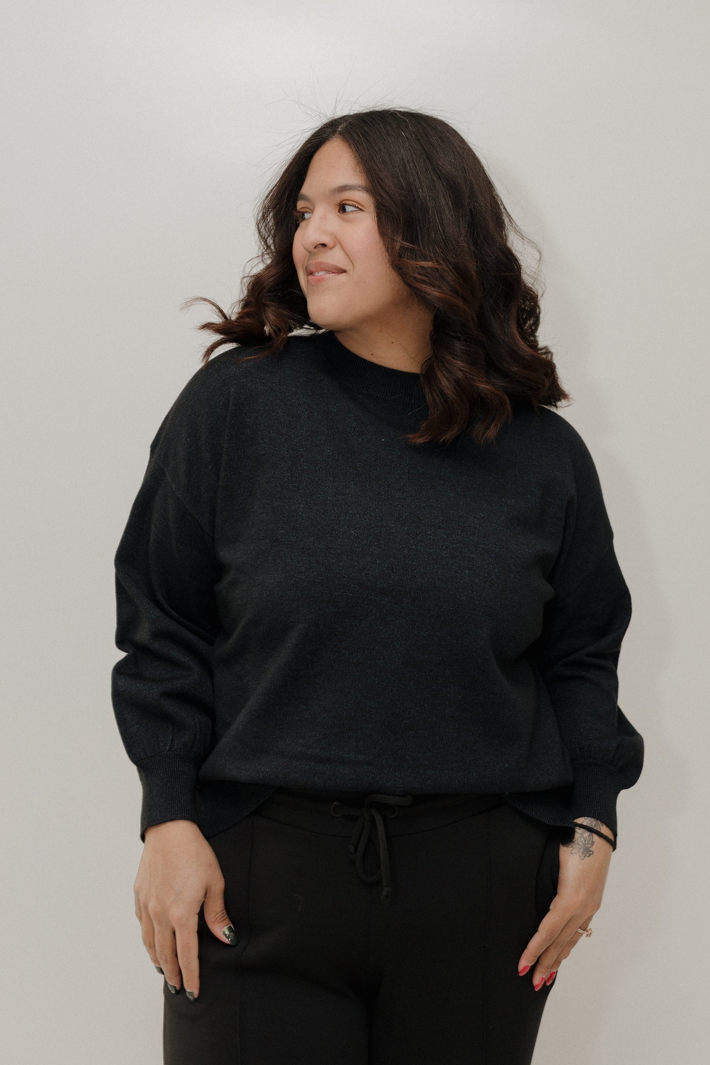 Person wearing a black sweater and pants against a plain background