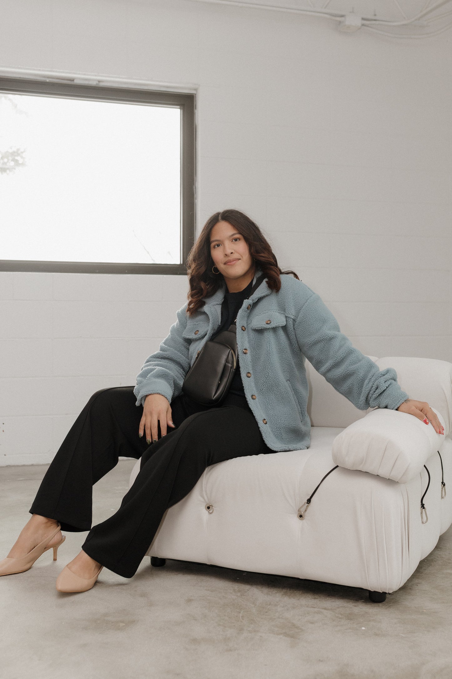 Woman sitting on a white chair in a minimalistic room with a large window.