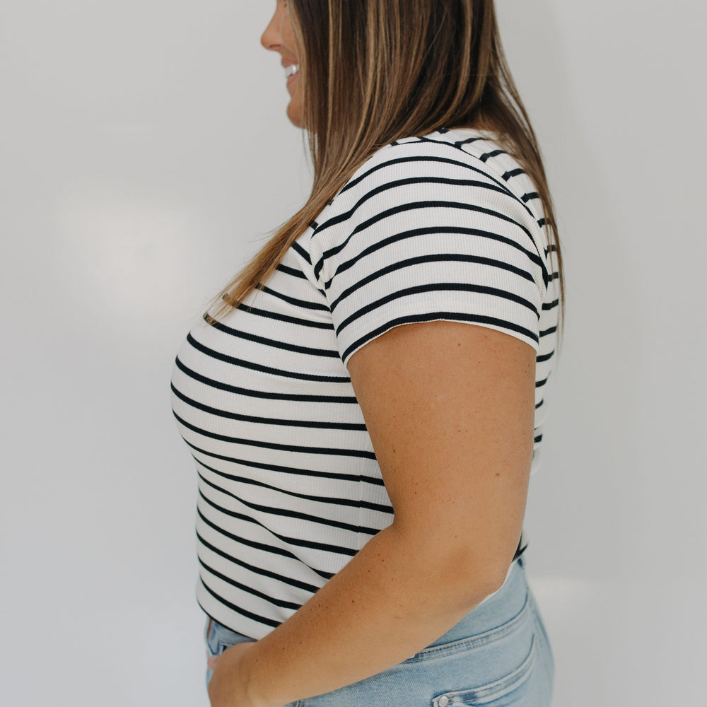 Woman wearing a black and white striped shirt and light blue jeans against a white background