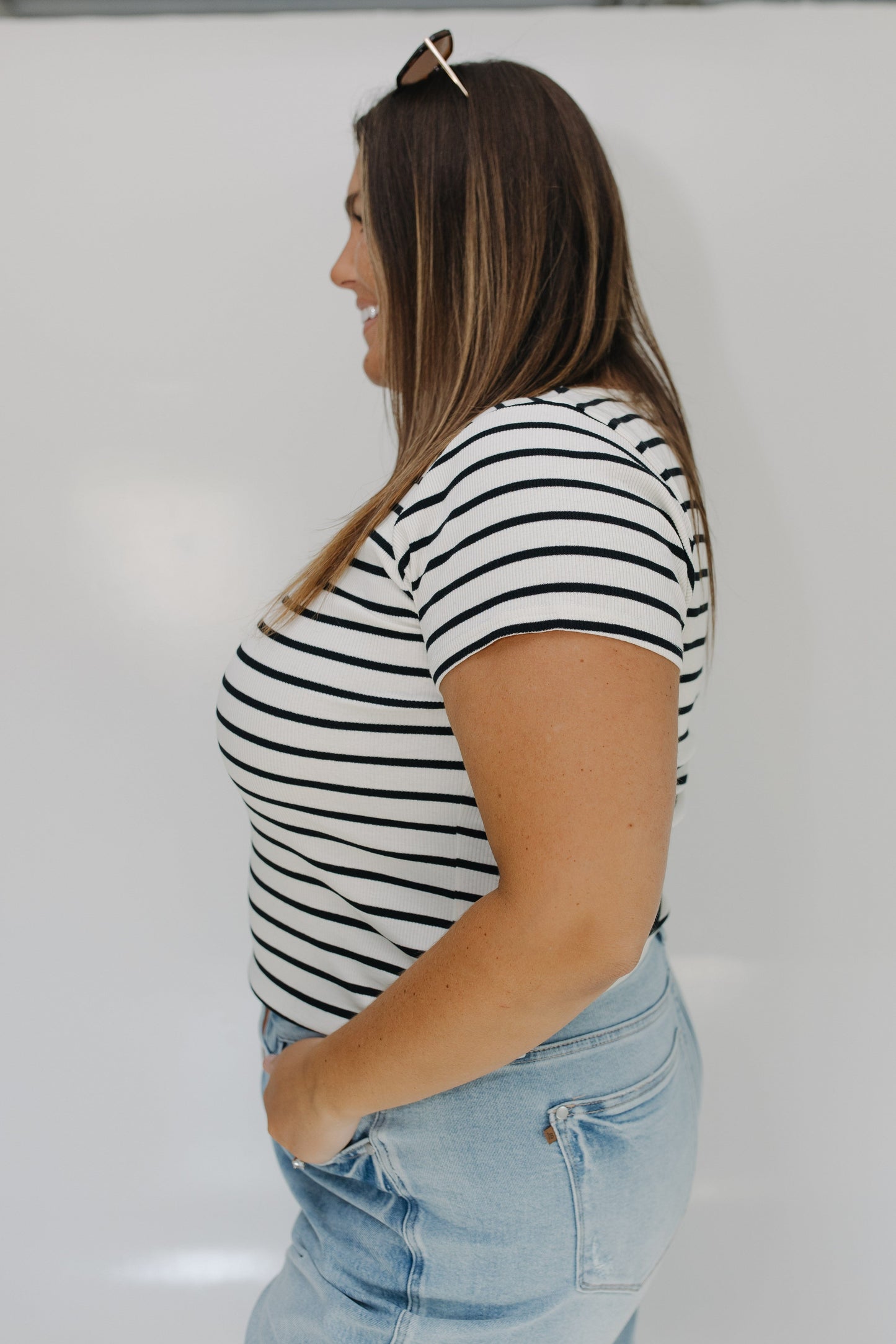 Woman wearing a black and white striped shirt and light blue jeans against a white background
