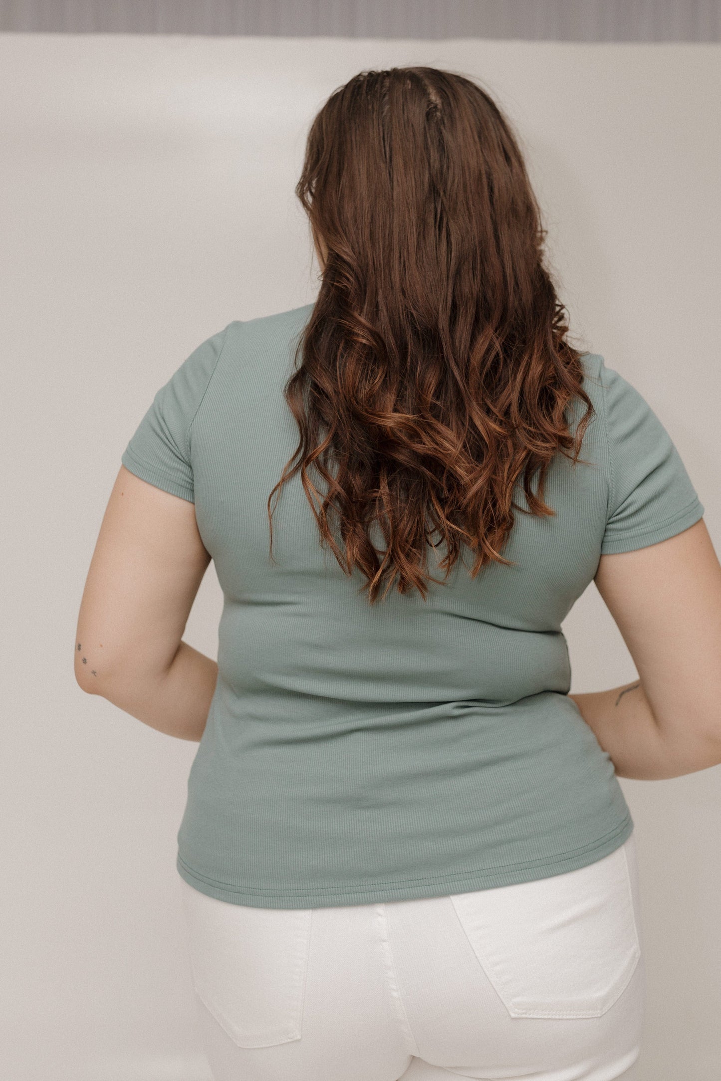 Person wearing a light green t-shirt and white pants against a plain background