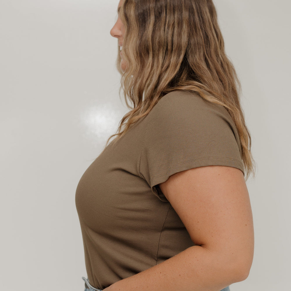 Woman wearing a brown t-shirt and blue jeans against a white background