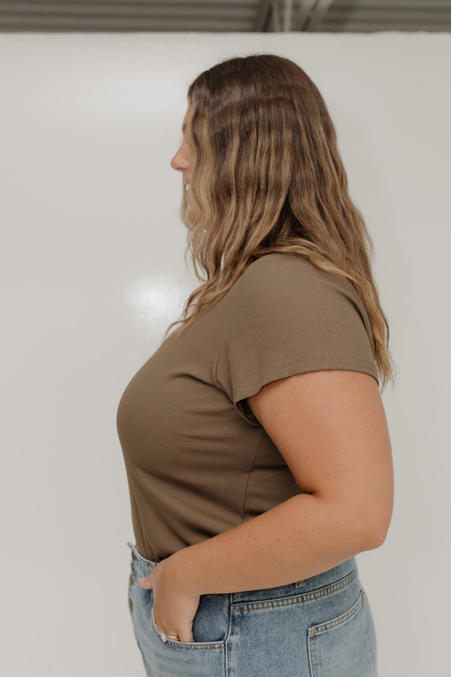 Woman wearing a brown t-shirt and blue jeans against a white background