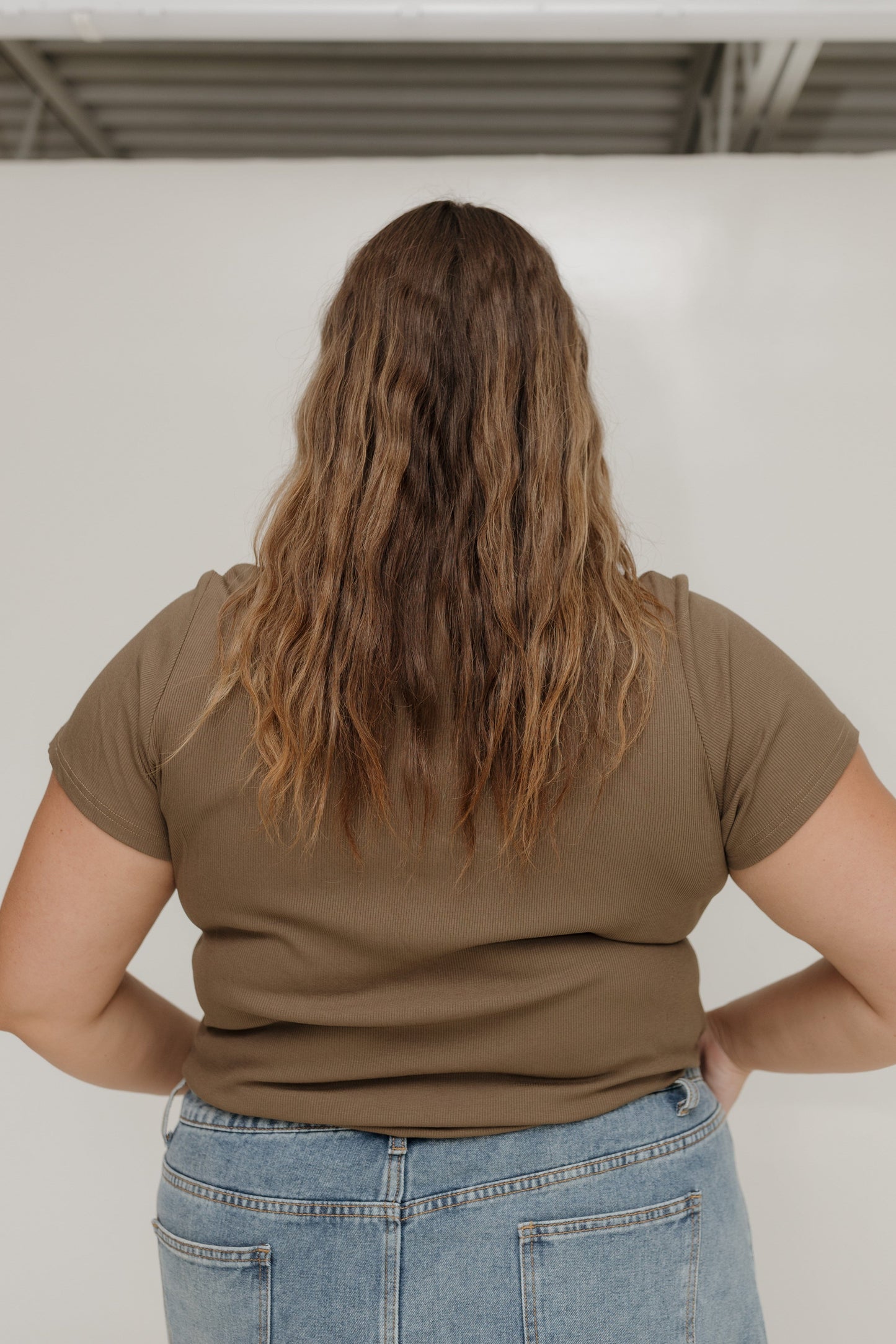 Person wearing a brown t-shirt and blue jeans with a plain background
