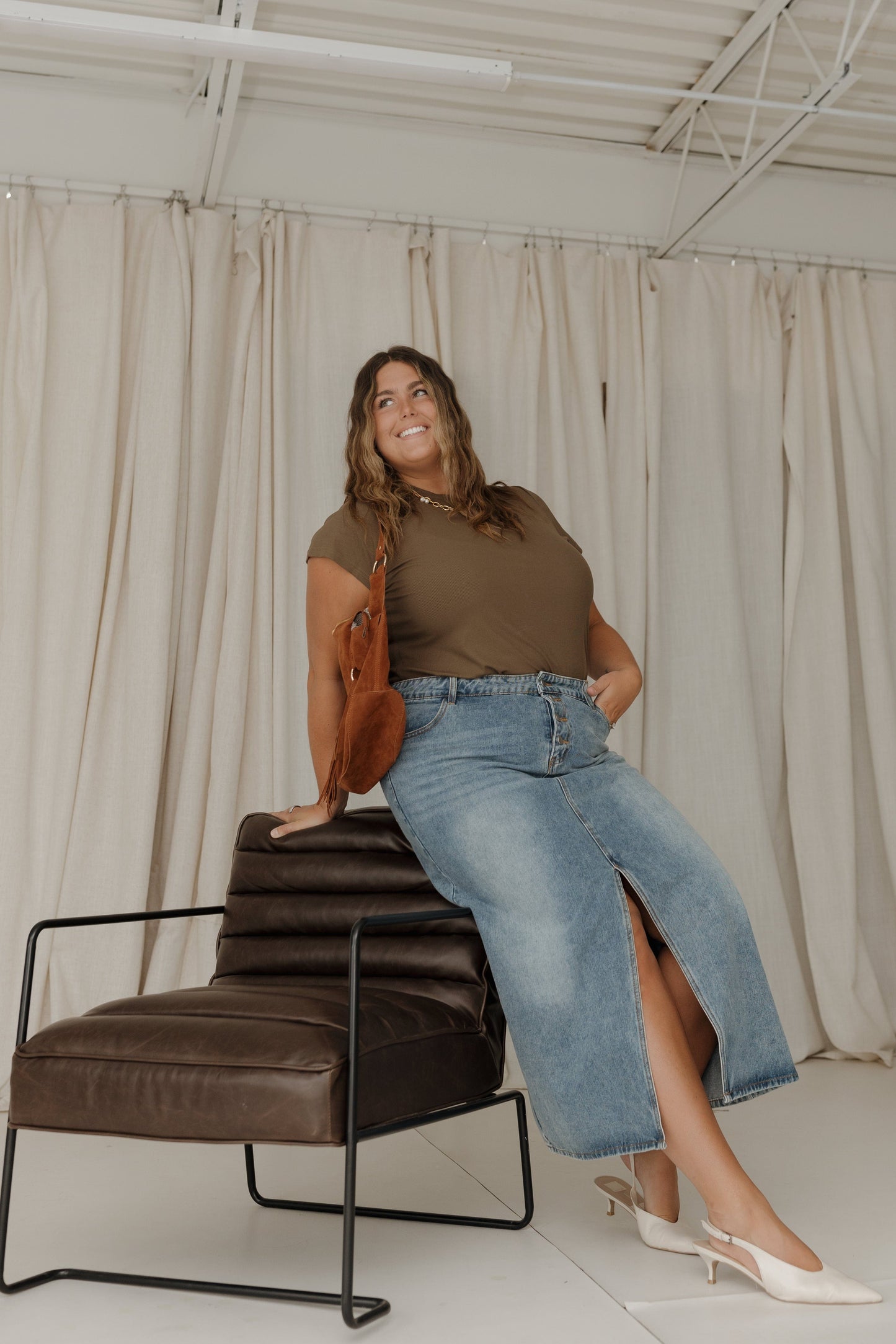 Woman sitting on a brown leather chair wearing a green top and blue jeans.