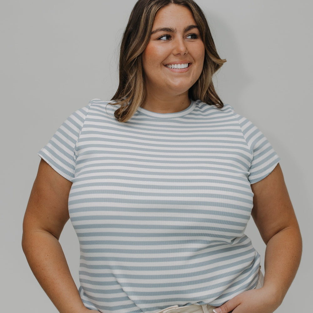 Woman wearing a striped t-shirt and beige pants against a plain background