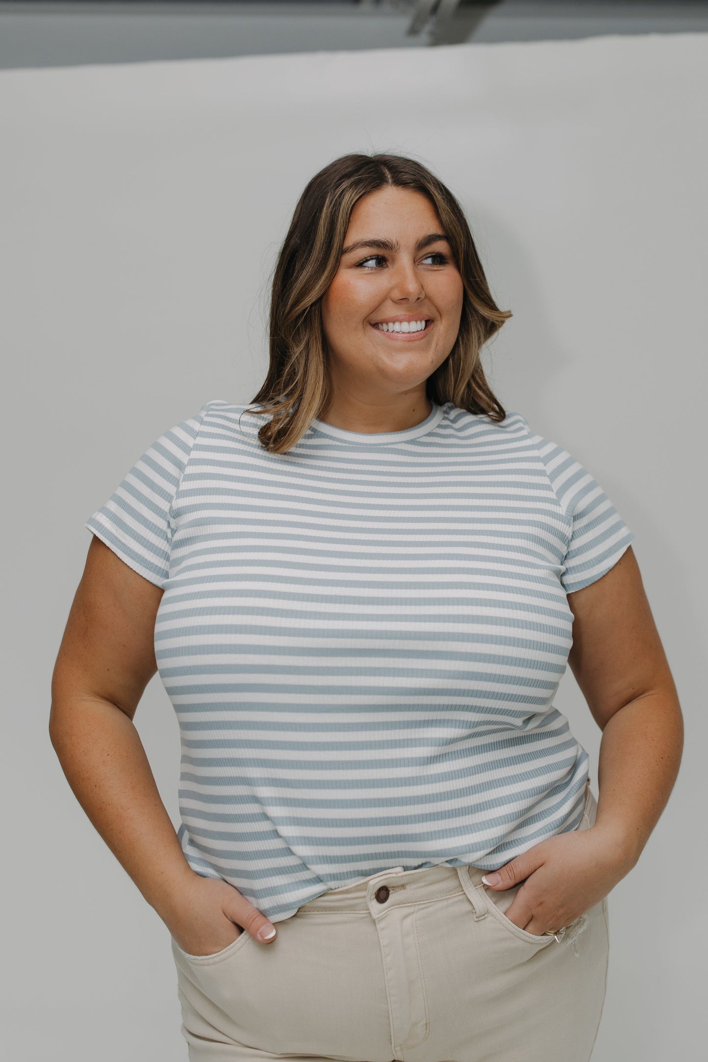 Woman wearing a striped t-shirt and beige pants against a plain background