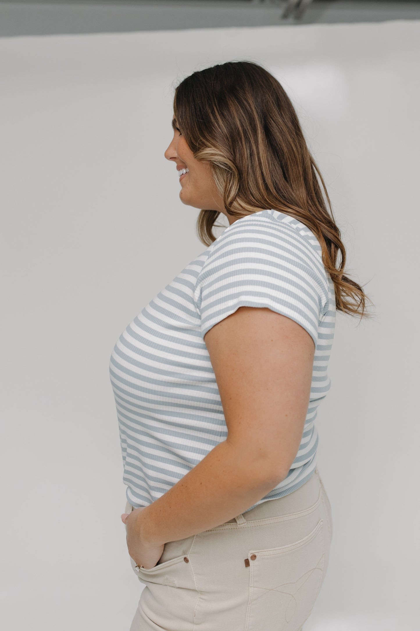 Woman wearing a striped shirt and beige pants against a white background