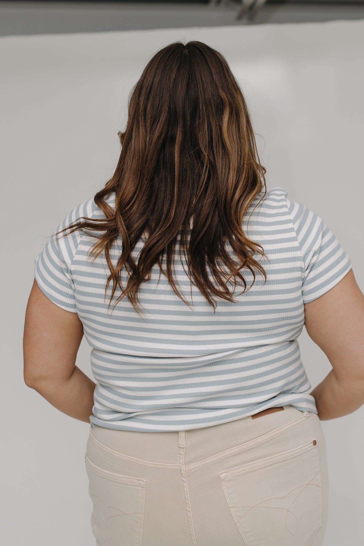 Person wearing a striped shirt and beige pants with a neutral background