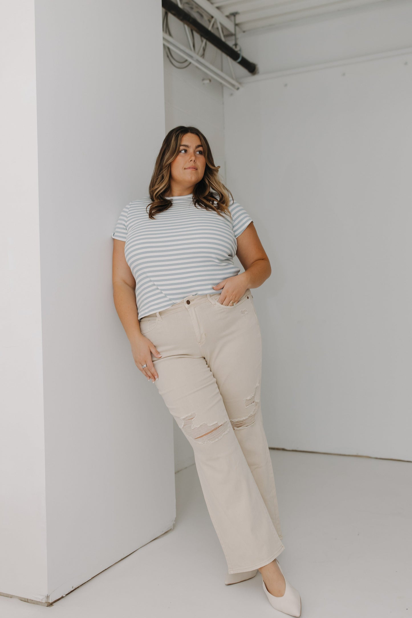 Woman wearing a striped shirt and beige pants in a minimal white room
