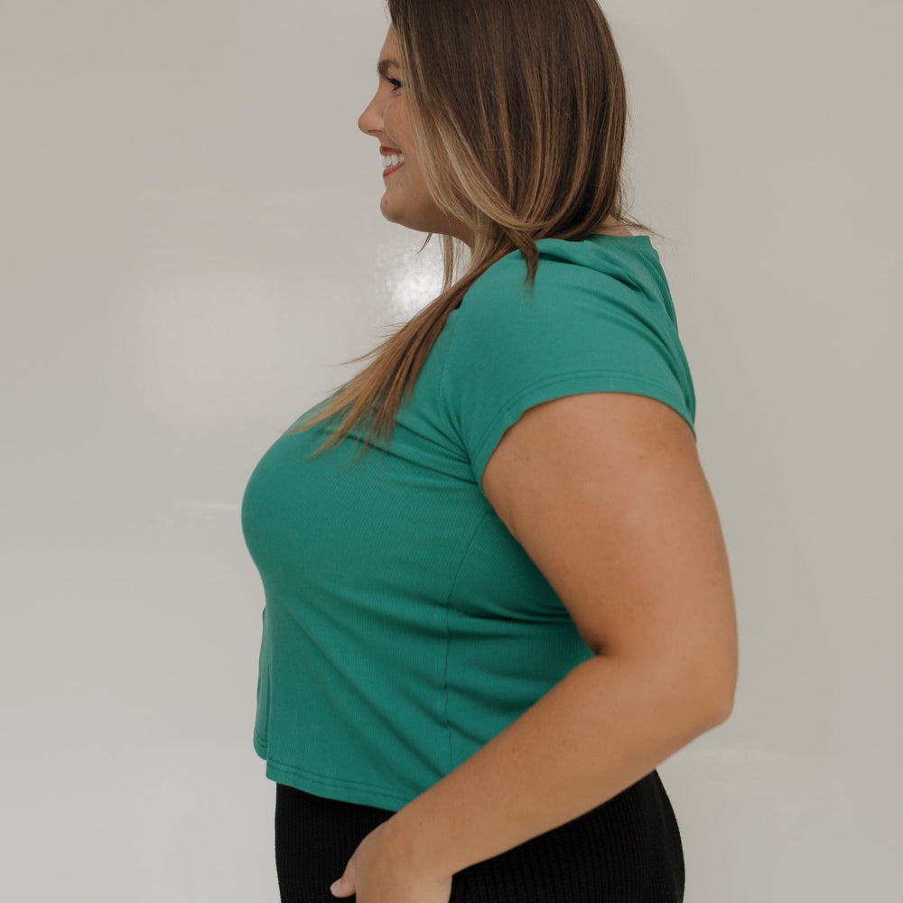 Woman wearing a green top and black pants against a white background