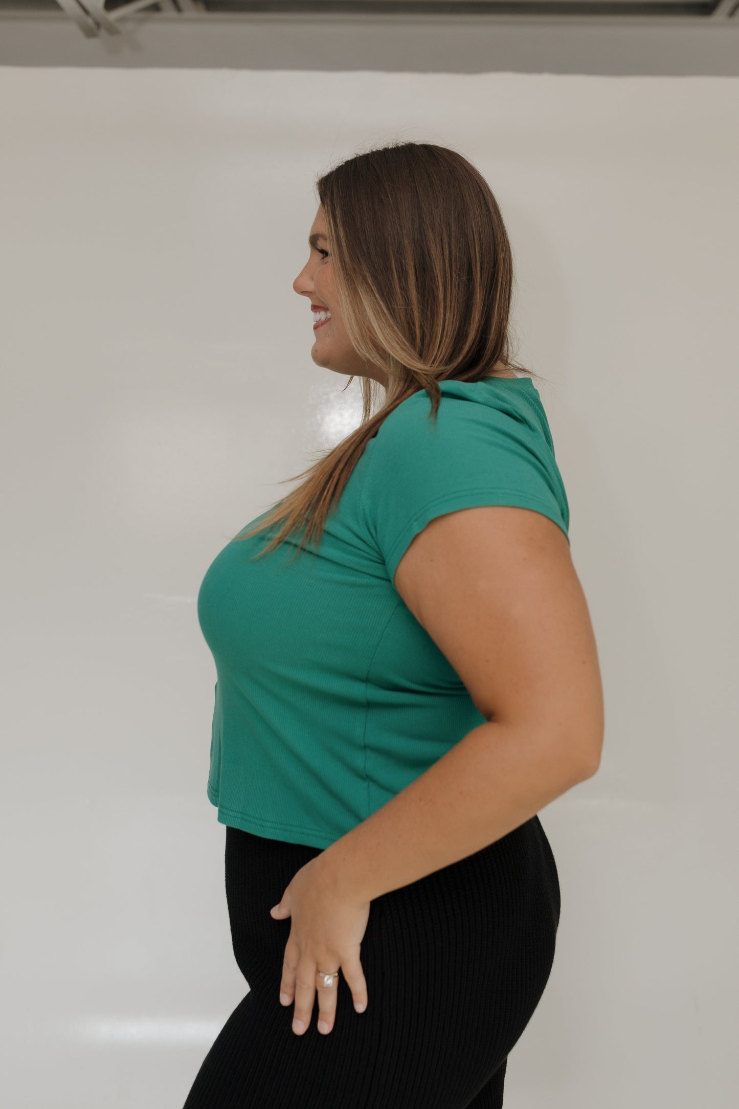 Woman wearing a green top and black pants against a white background