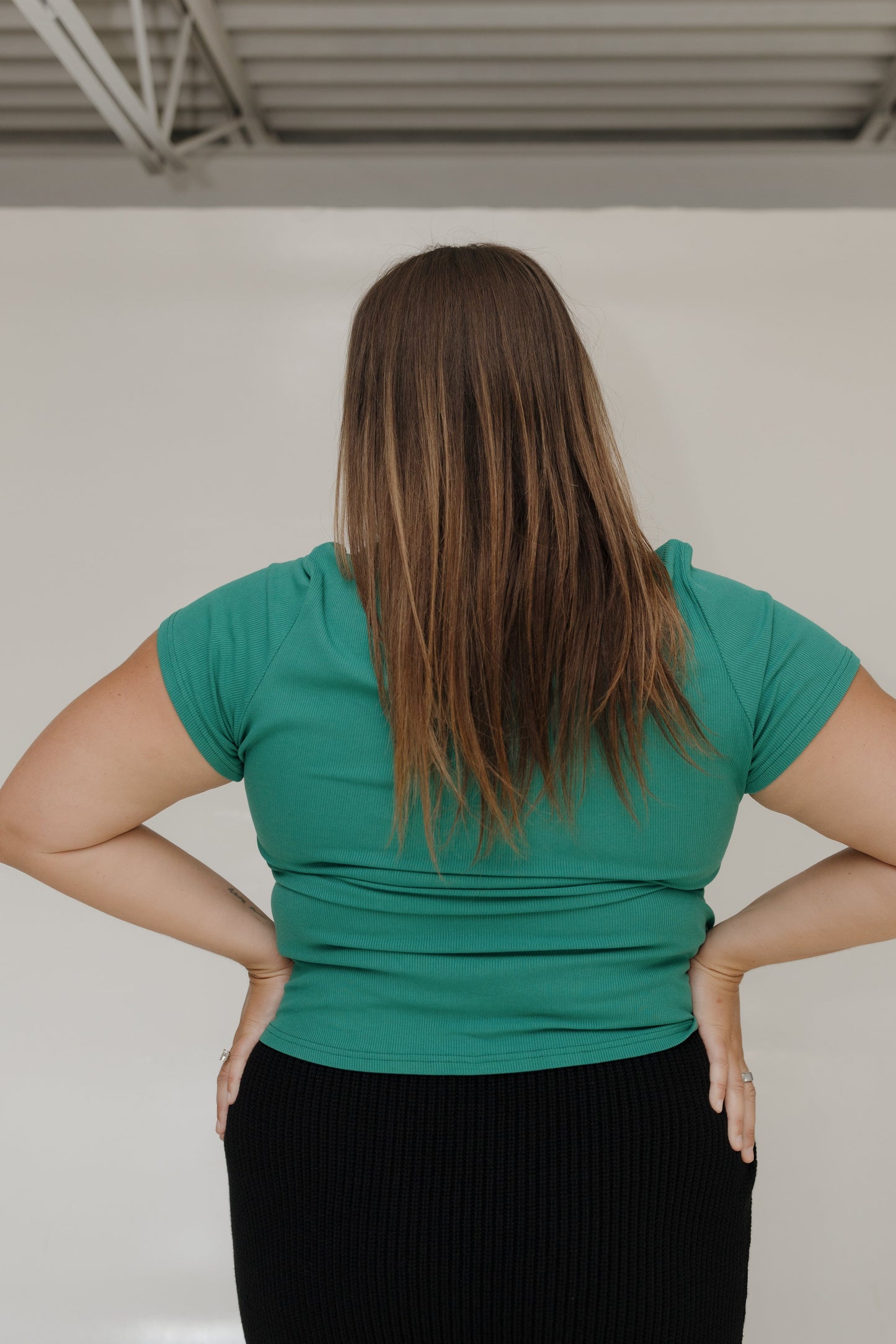 Person wearing a green shirt with hands on hips against a plain background