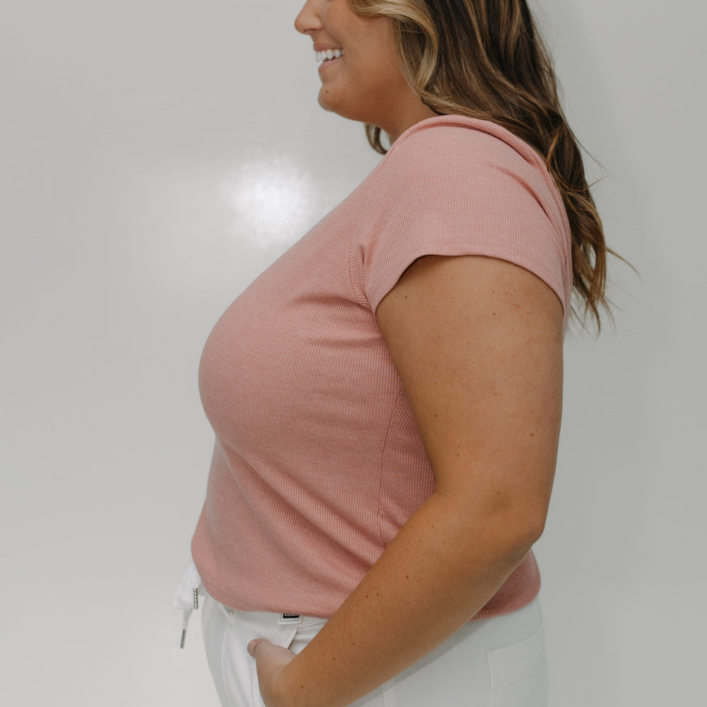 Woman wearing a pink t-shirt and white pants against a plain background