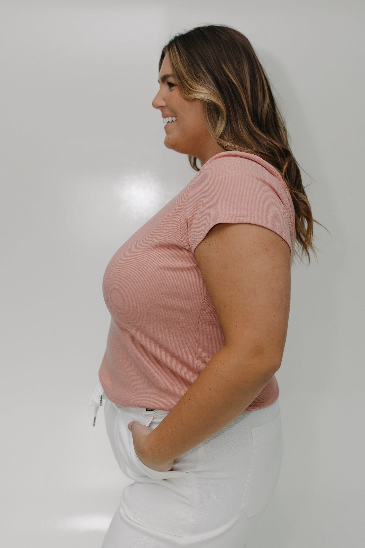 Woman wearing a pink t-shirt and white pants against a plain background