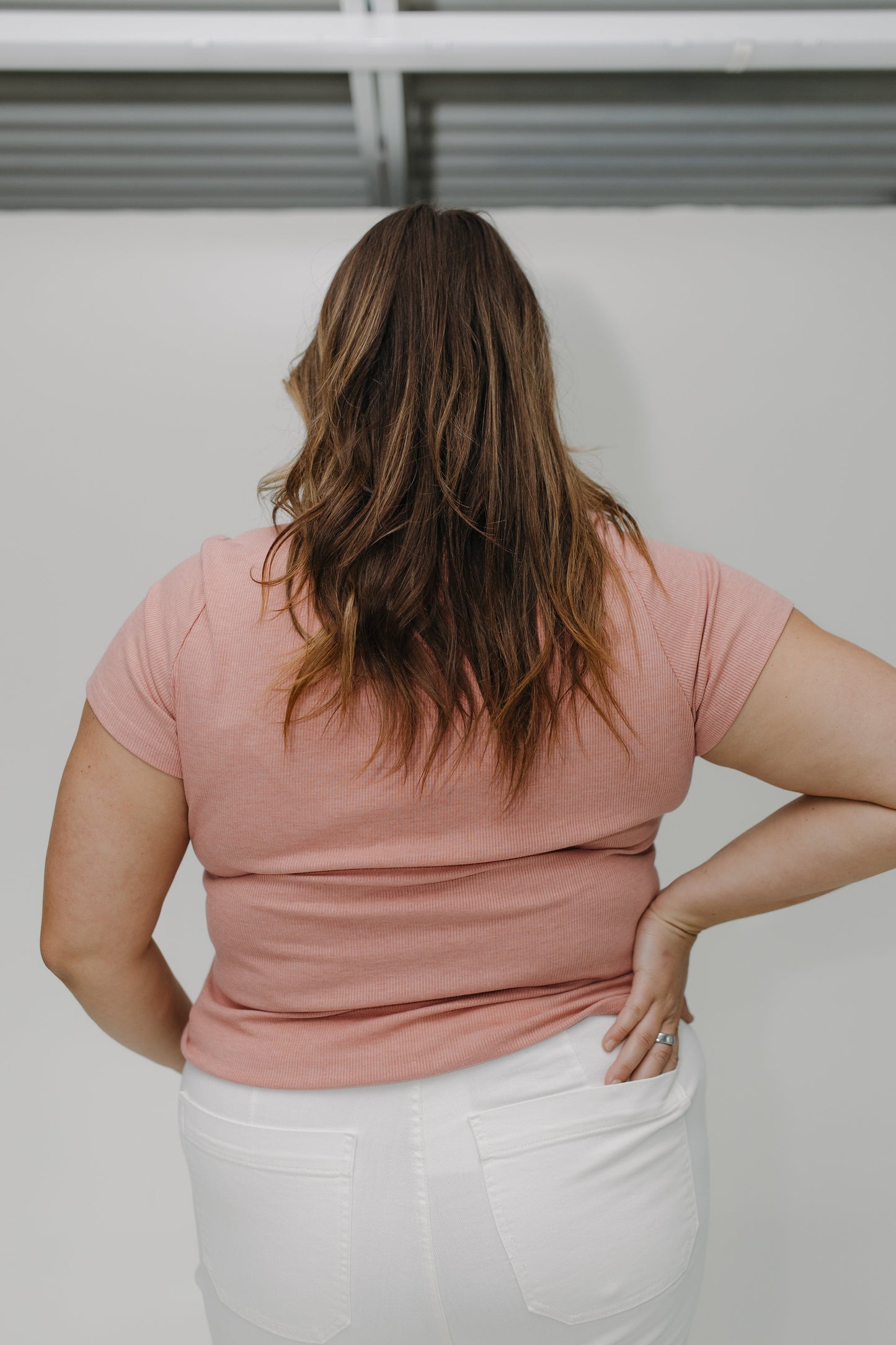 Person wearing a pink shirt and white pants against a plain background