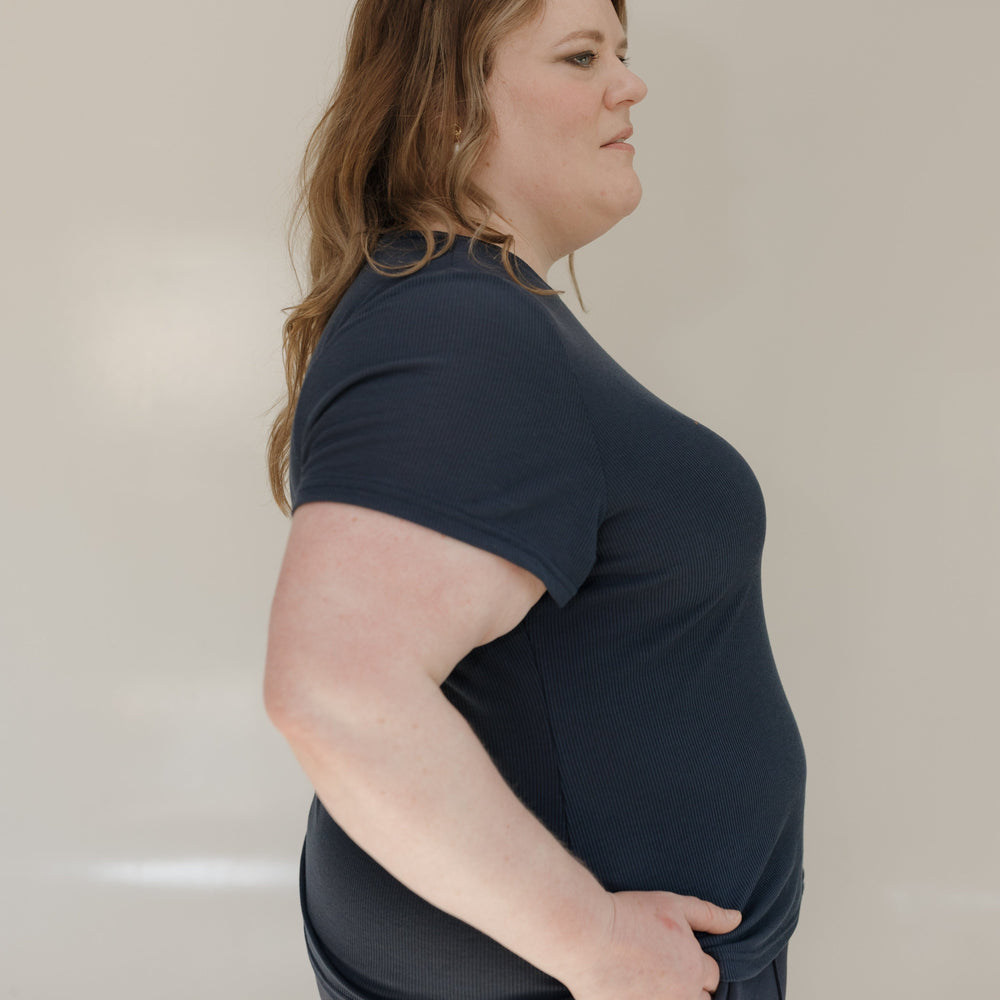 Woman wearing a navy blue t-shirt and gray pants against a plain background