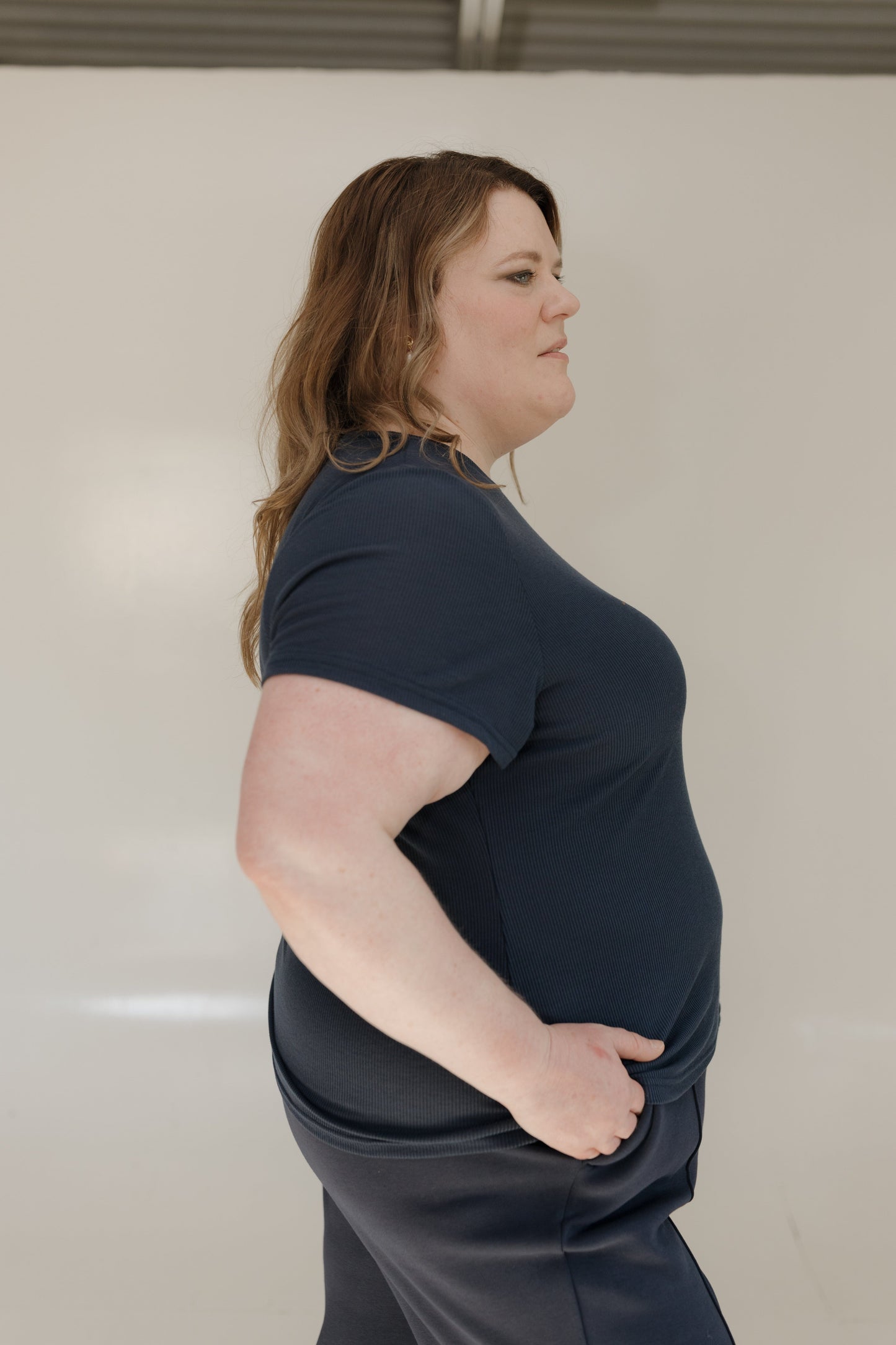 Woman wearing a navy blue t-shirt and gray pants against a plain background