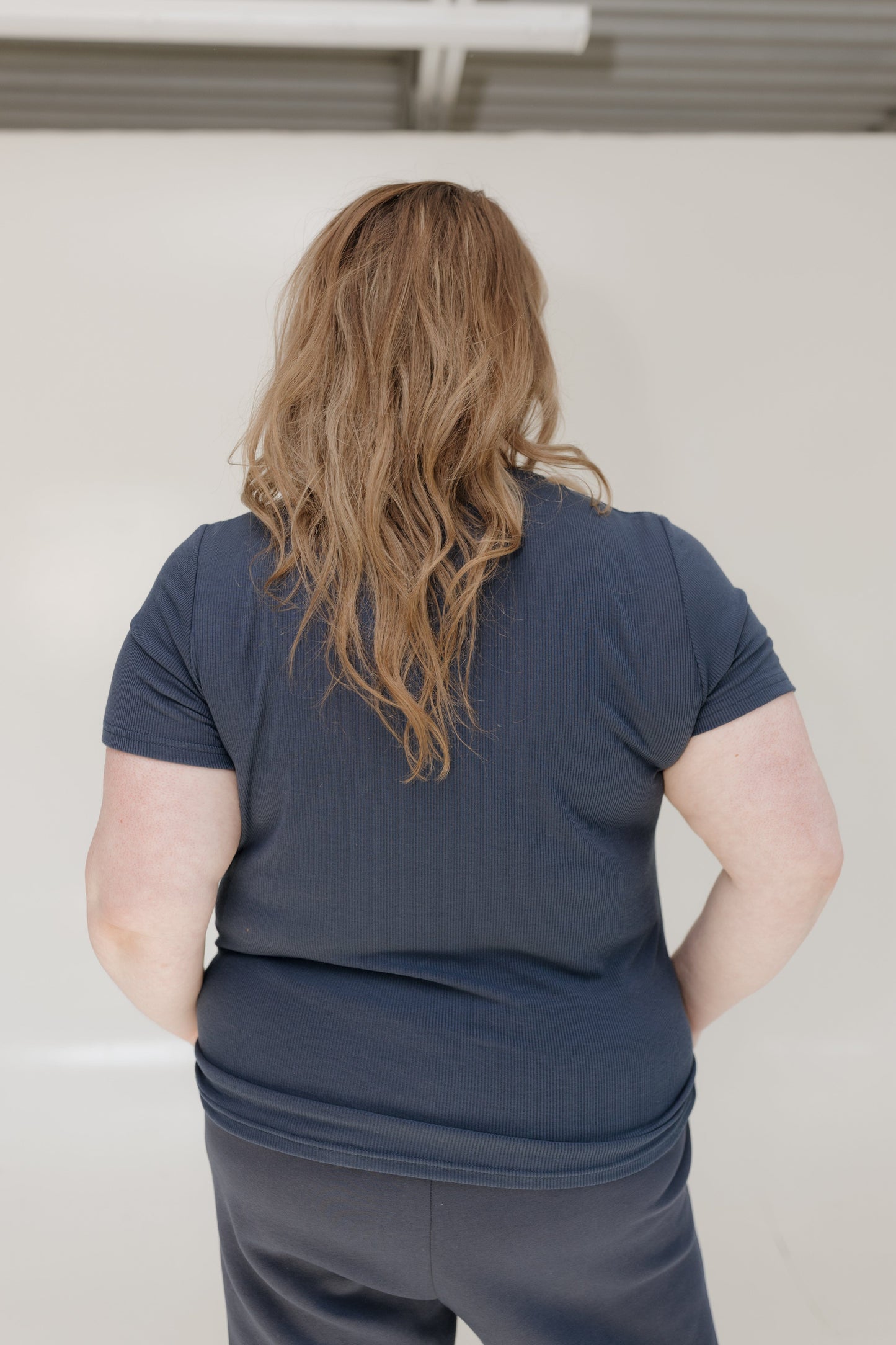 Person wearing a blue shirt and pants standing against a plain white wall.