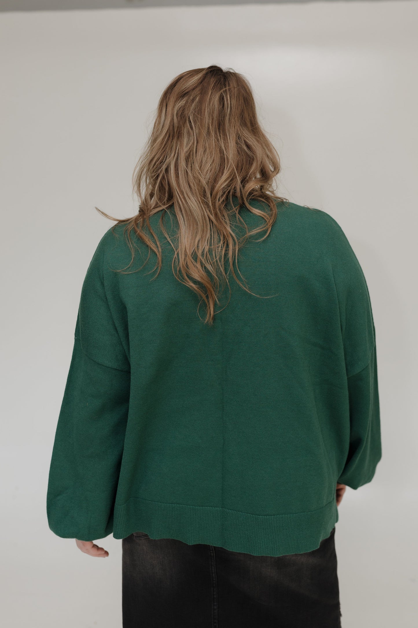 Person wearing a green sweater from behind on a plain background