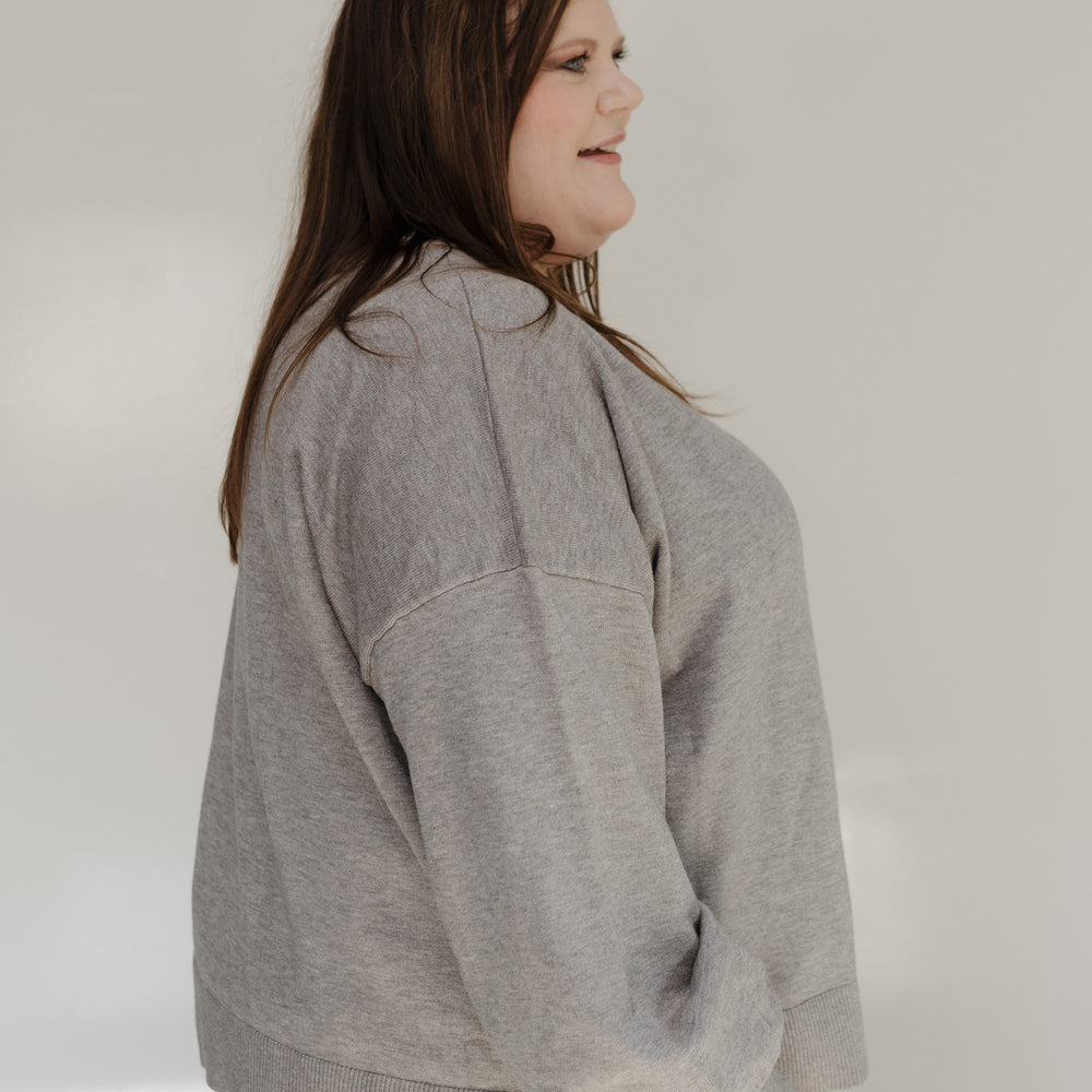 Person wearing a gray sweatshirt and light blue jeans against a plain background