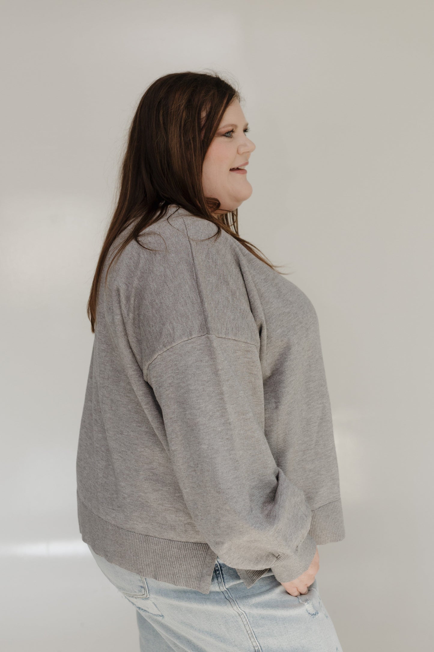 Person wearing a gray sweatshirt and light blue jeans against a plain background