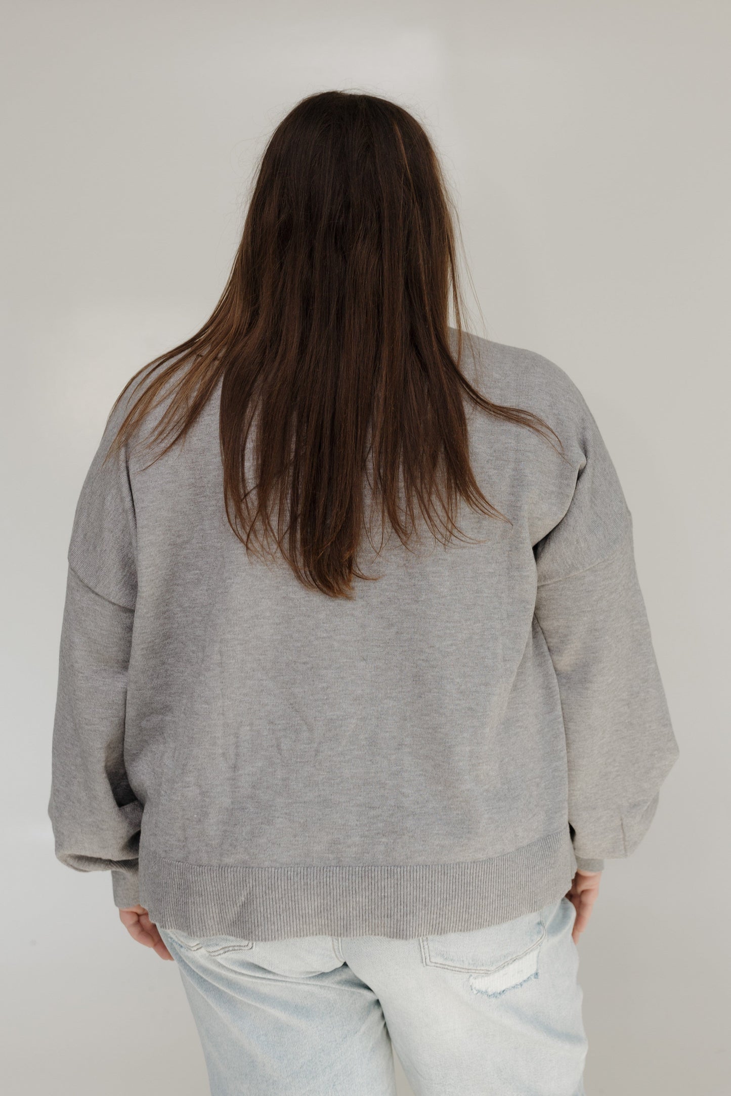 Person wearing a gray sweater and light blue jeans against a plain background