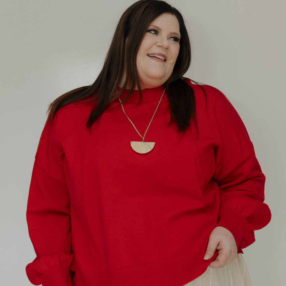 Woman wearing a red sweater and beige skirt against a plain background