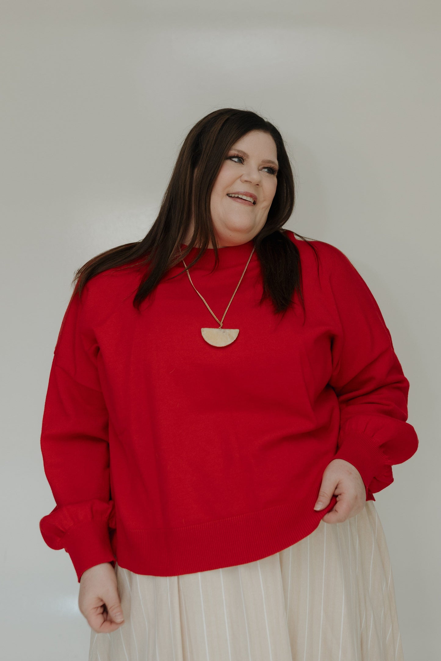 Woman wearing a red sweater and beige skirt against a plain background