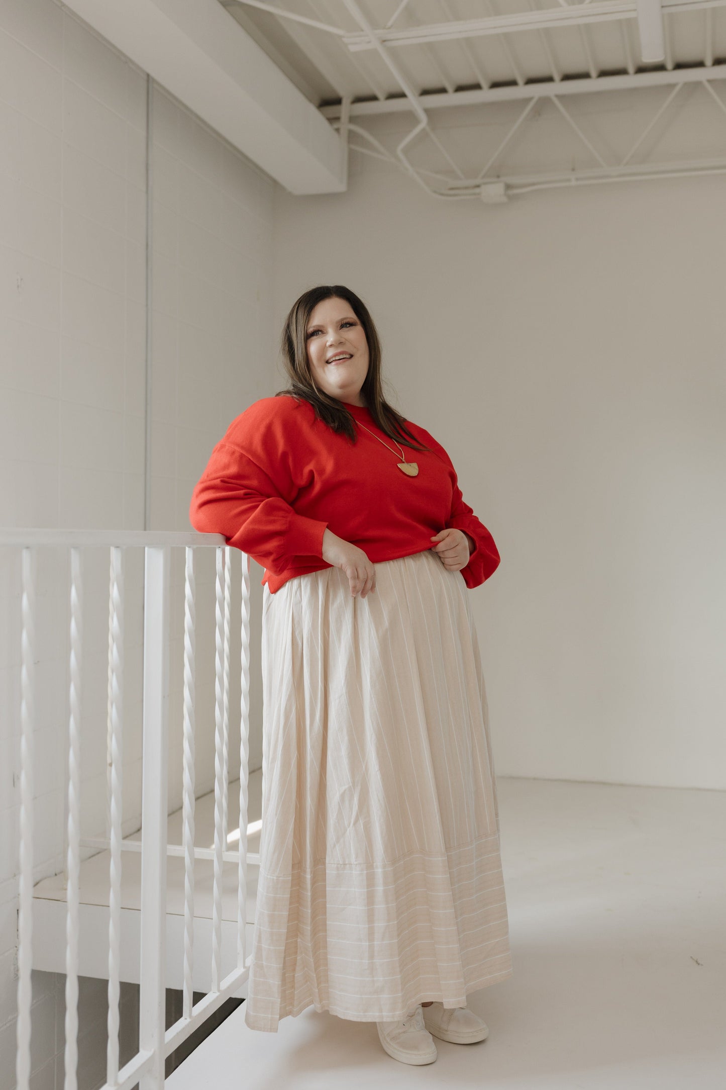 Person wearing a red sweater and beige skirt standing in a minimalistic room.
