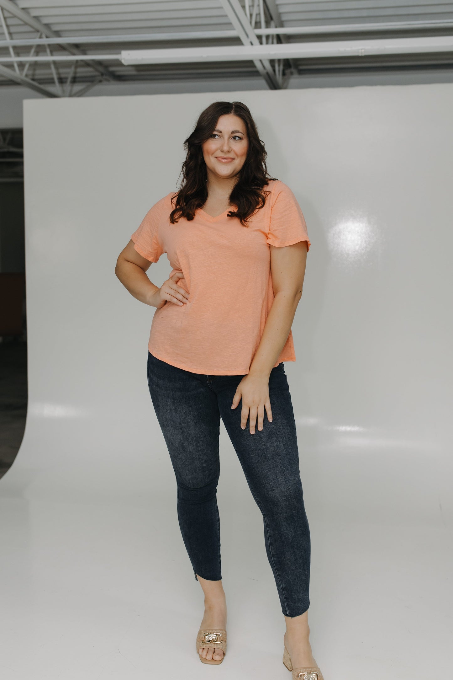 Woman wearing a peach top and dark jeans in a studio setting