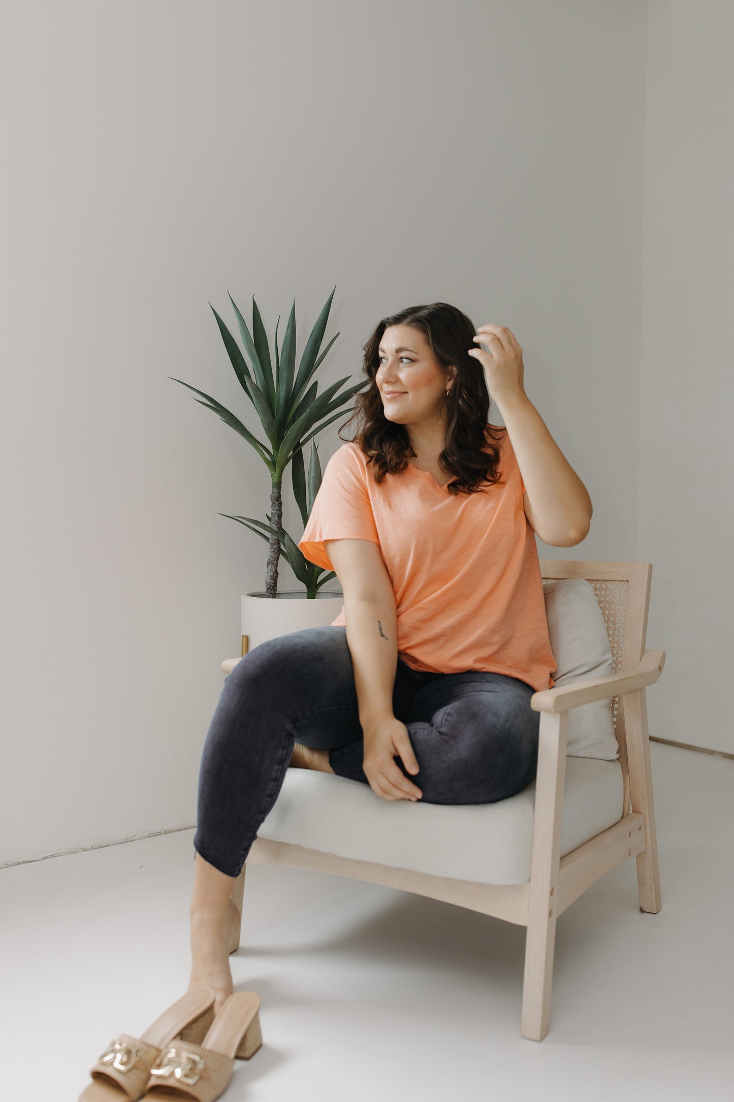 Woman sitting on a chair in a minimalistic room with a plant in the background