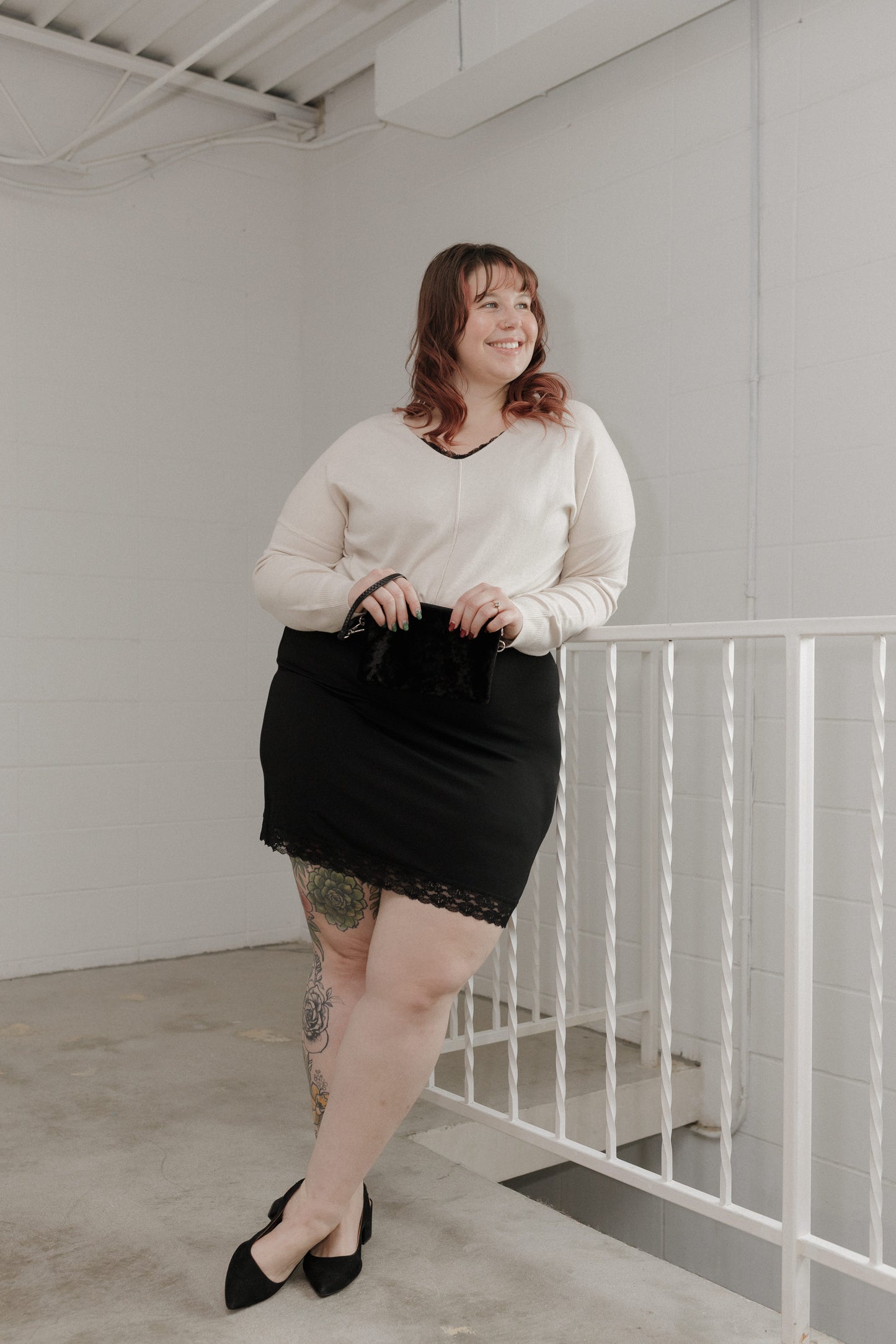Woman in a white blouse and black skirt standing in a minimalistic room.