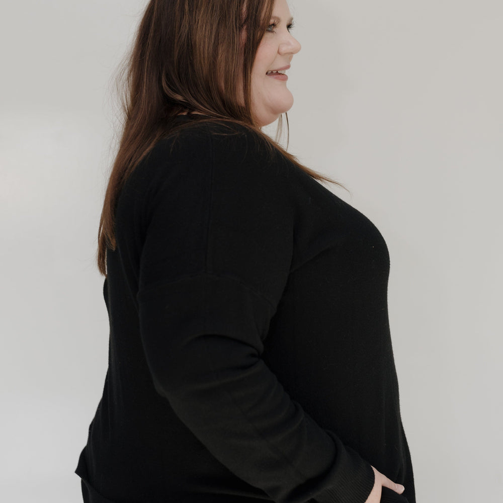 Person wearing a black top and light blue jeans against a white wall