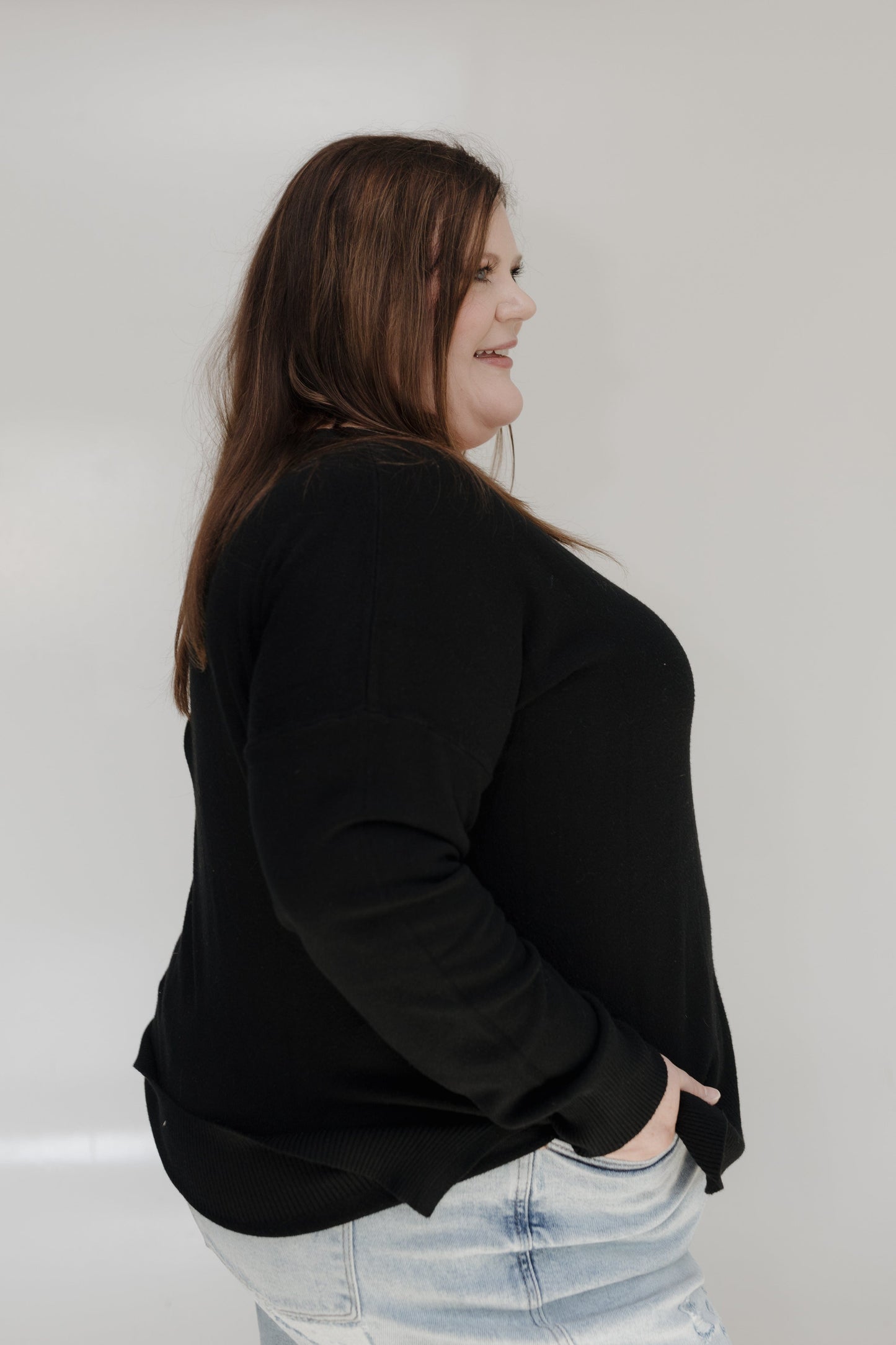 Person wearing a black top and light blue jeans against a white wall