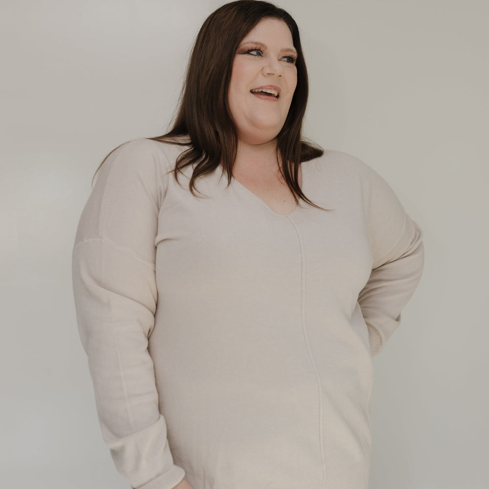 Woman wearing a beige sweater standing against a white wall