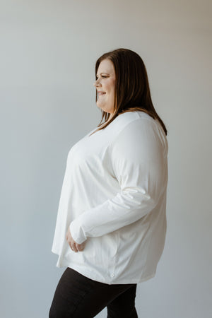 A person dressed in a Yesta ESSENTIAL V-NECK LIGHTWEIGHT BLOUSE IN ECRU and dark pants stands in profile against a plain background.