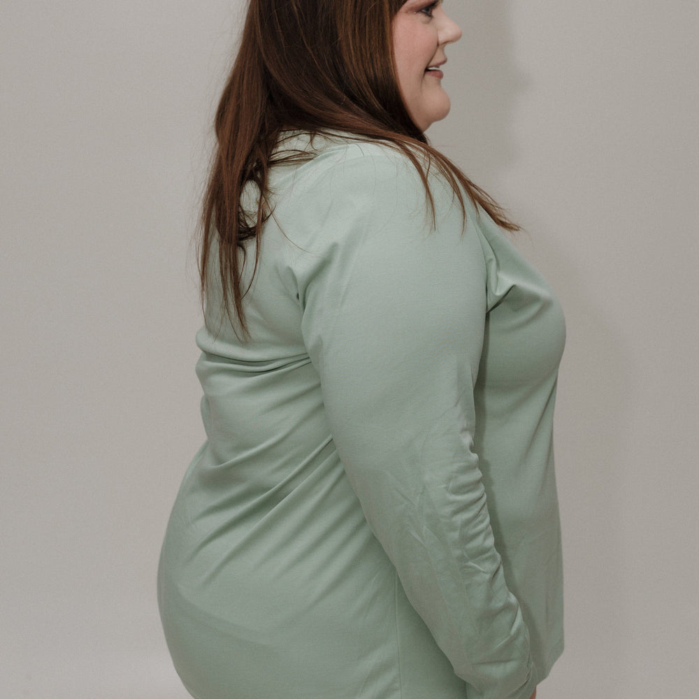 Woman wearing a light green long-sleeve shirt against a plain background