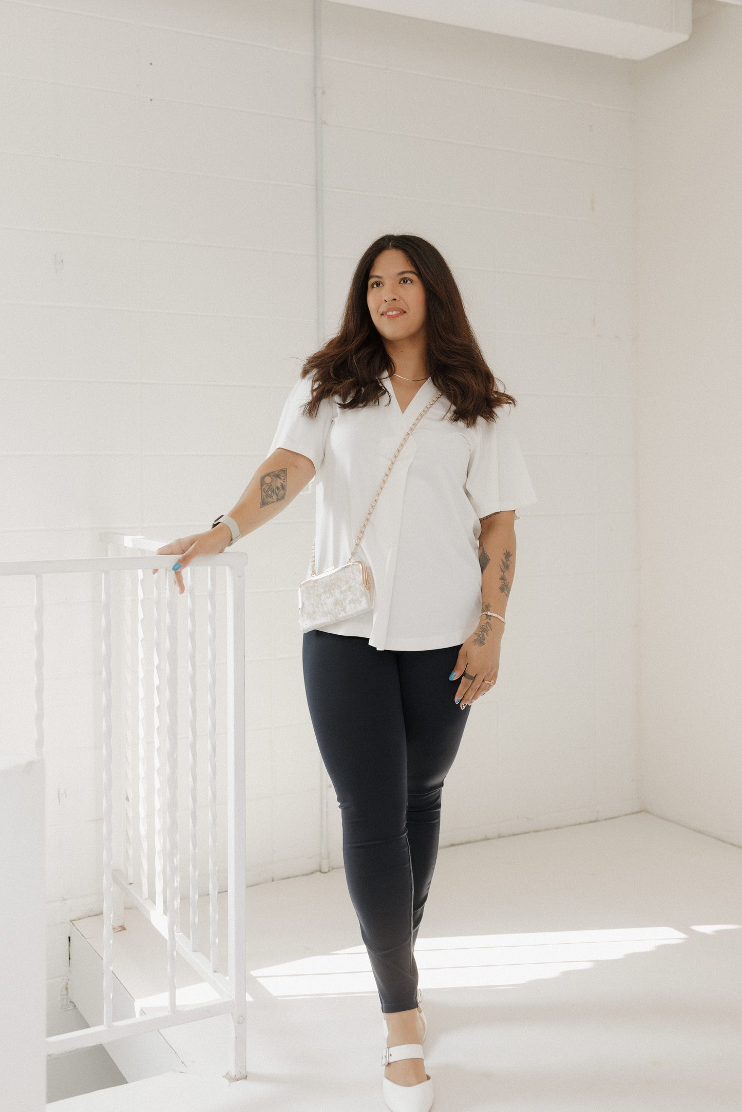 Woman in a white shirt and black pants standing in a bright, minimalistic room.