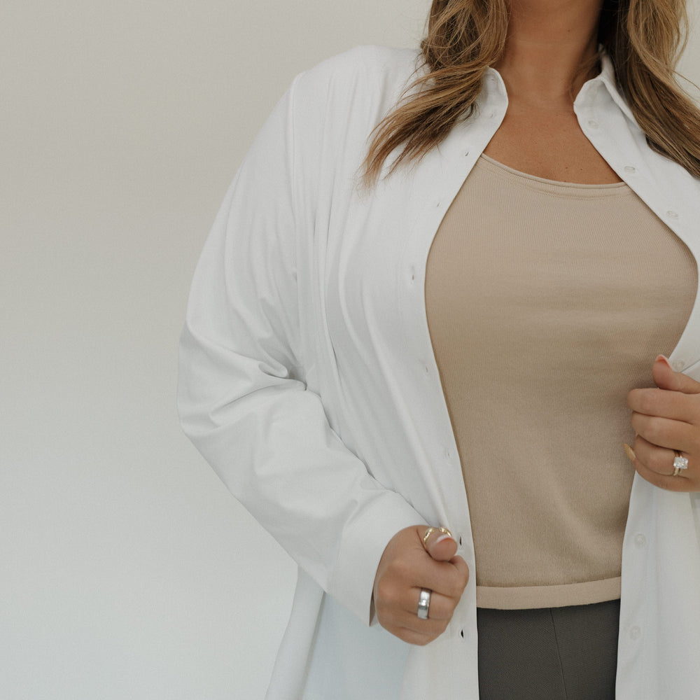 Woman wearing a white cardigan over a beige top with a neutral background