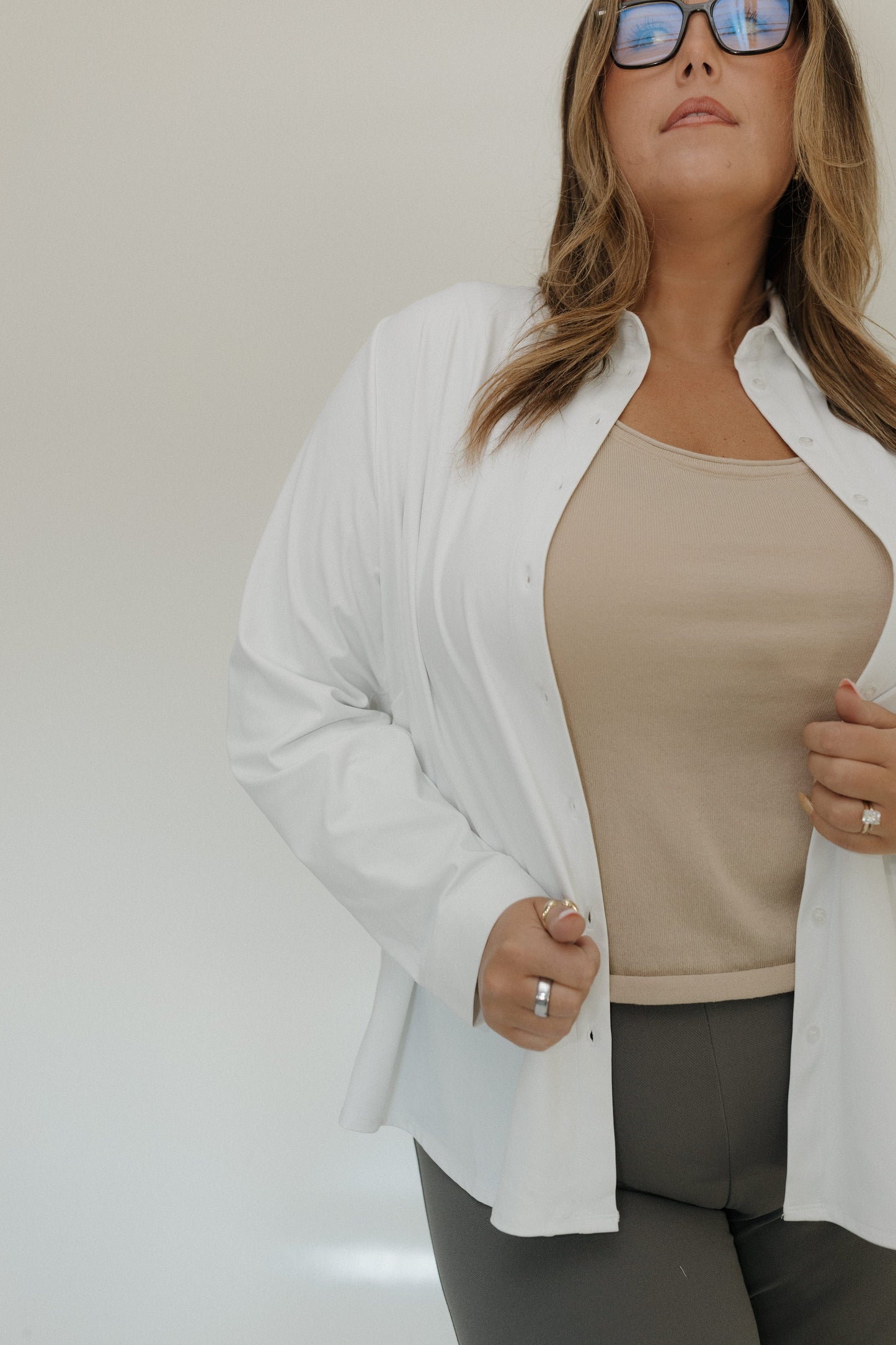 Woman wearing a white cardigan over a beige top with a neutral background