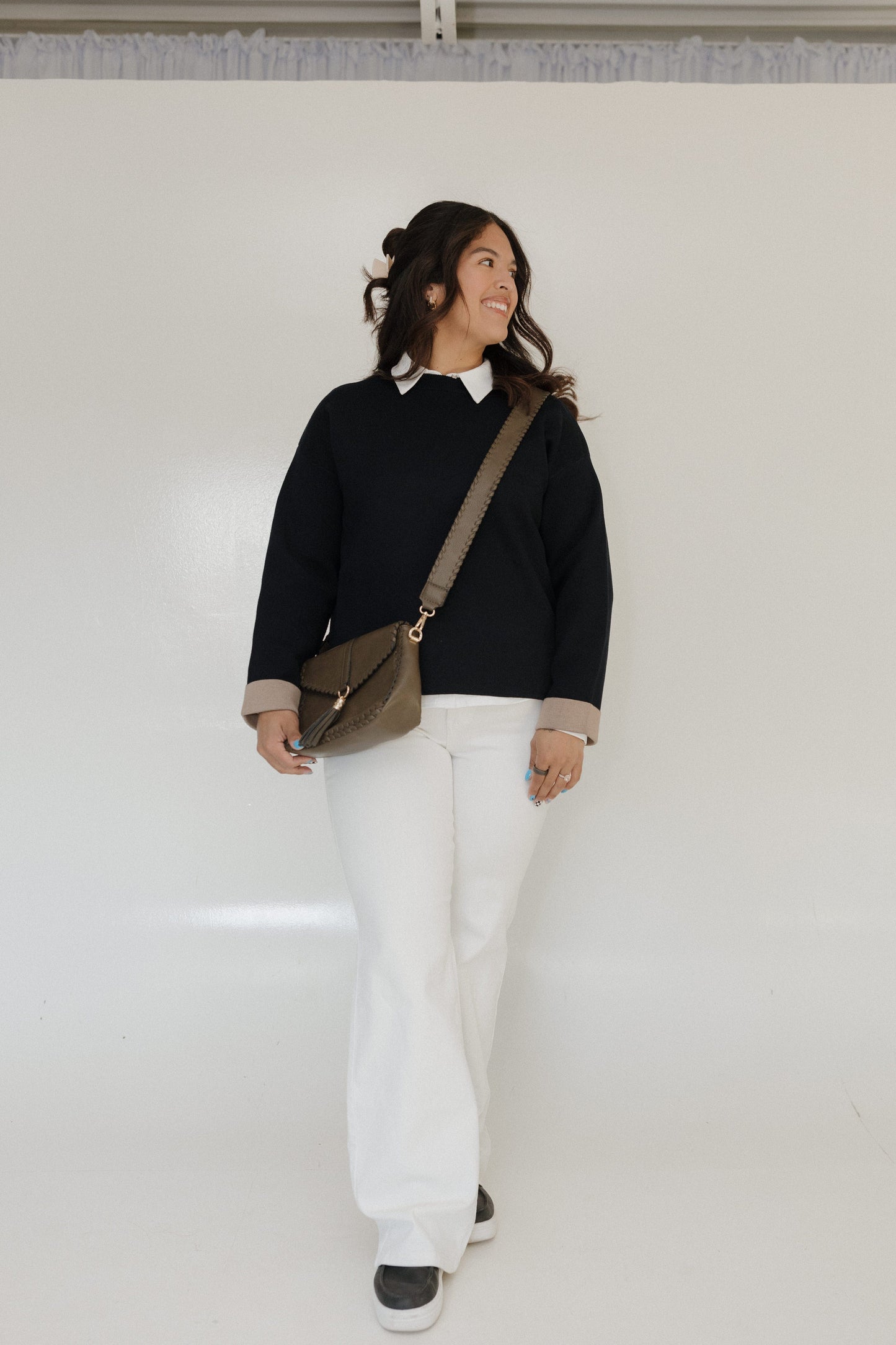 Person wearing a black sweater, white pants, and carrying a brown bag against a white background