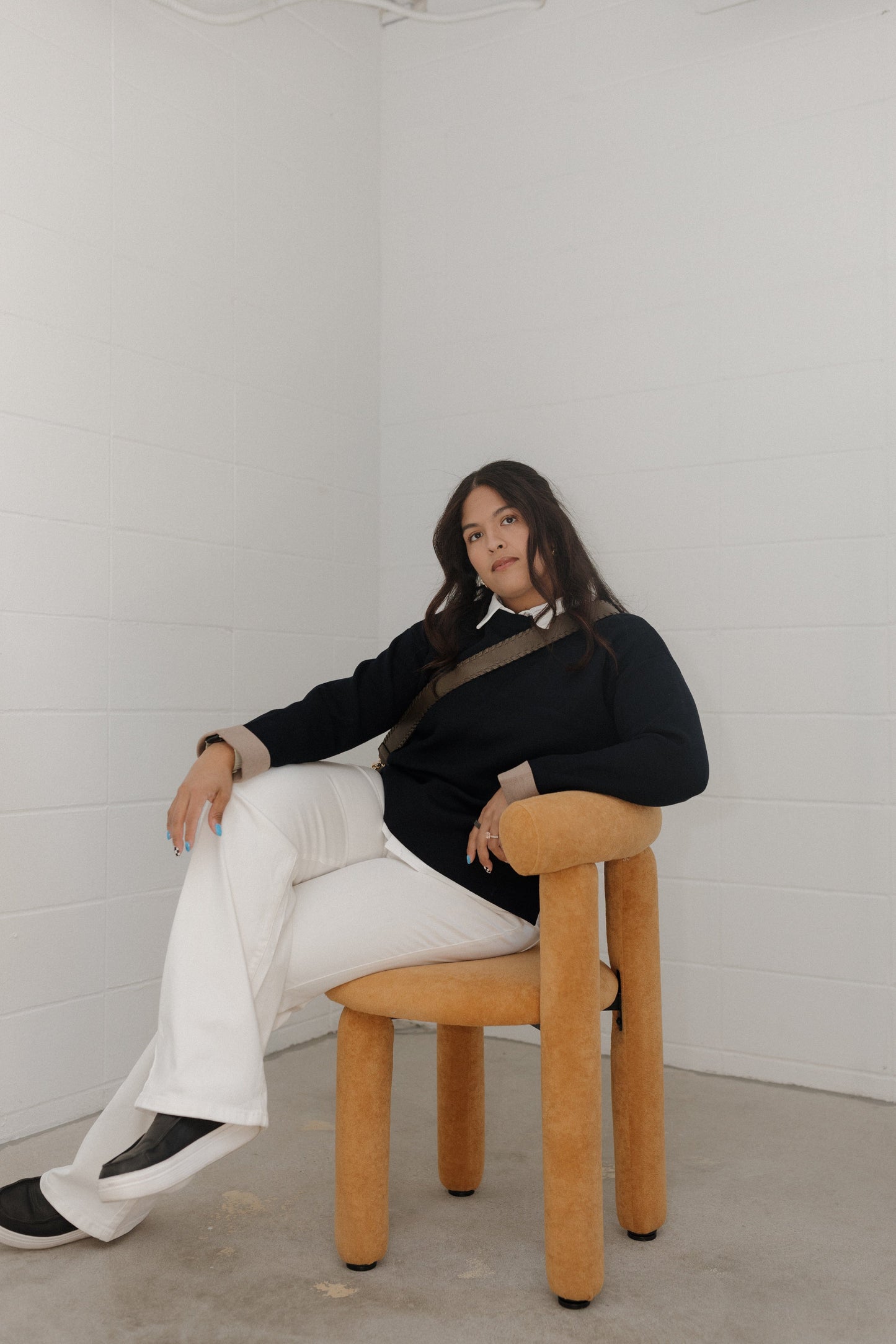 Woman sitting on a wooden chair against a white wall