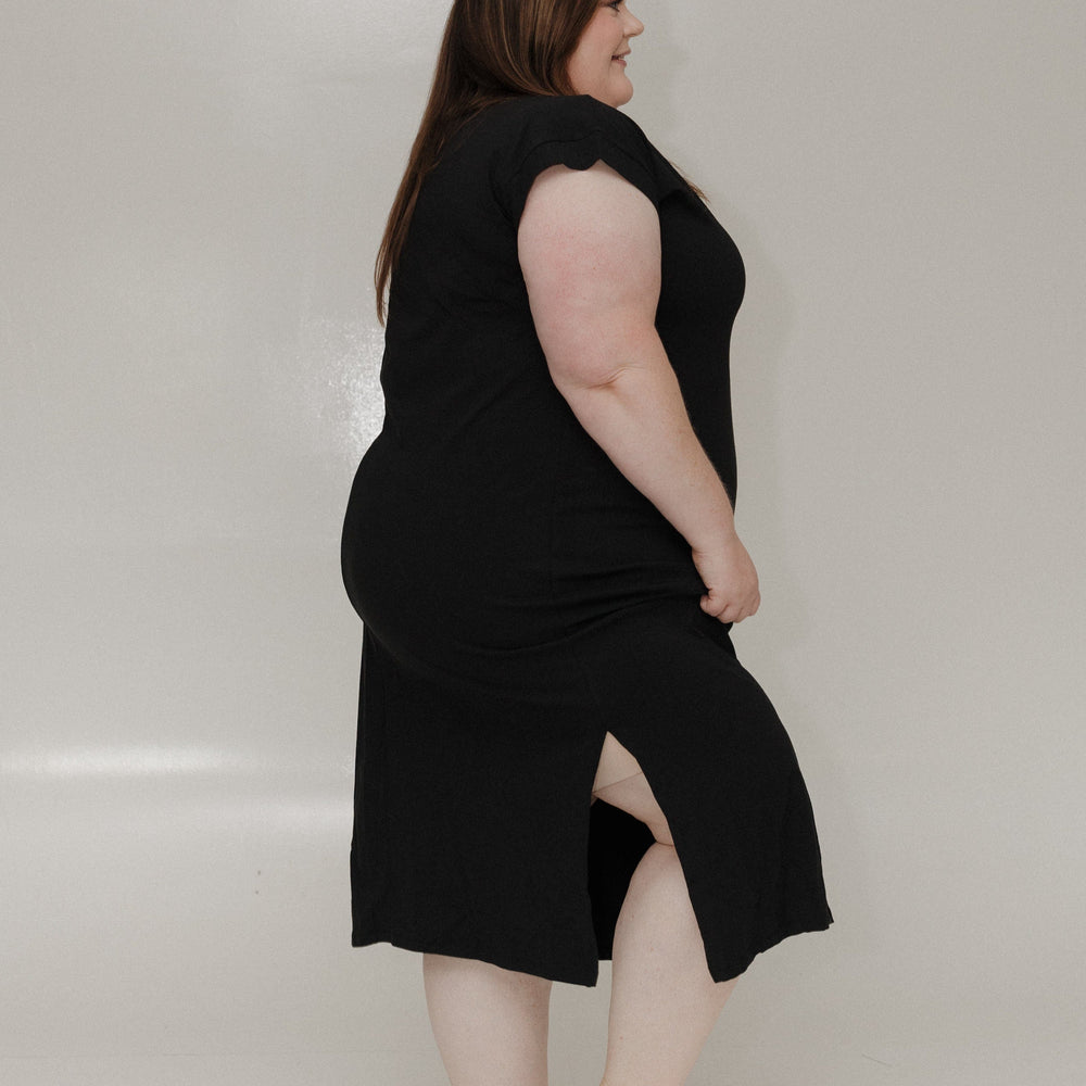 Woman wearing a black sleeveless dress against a plain background