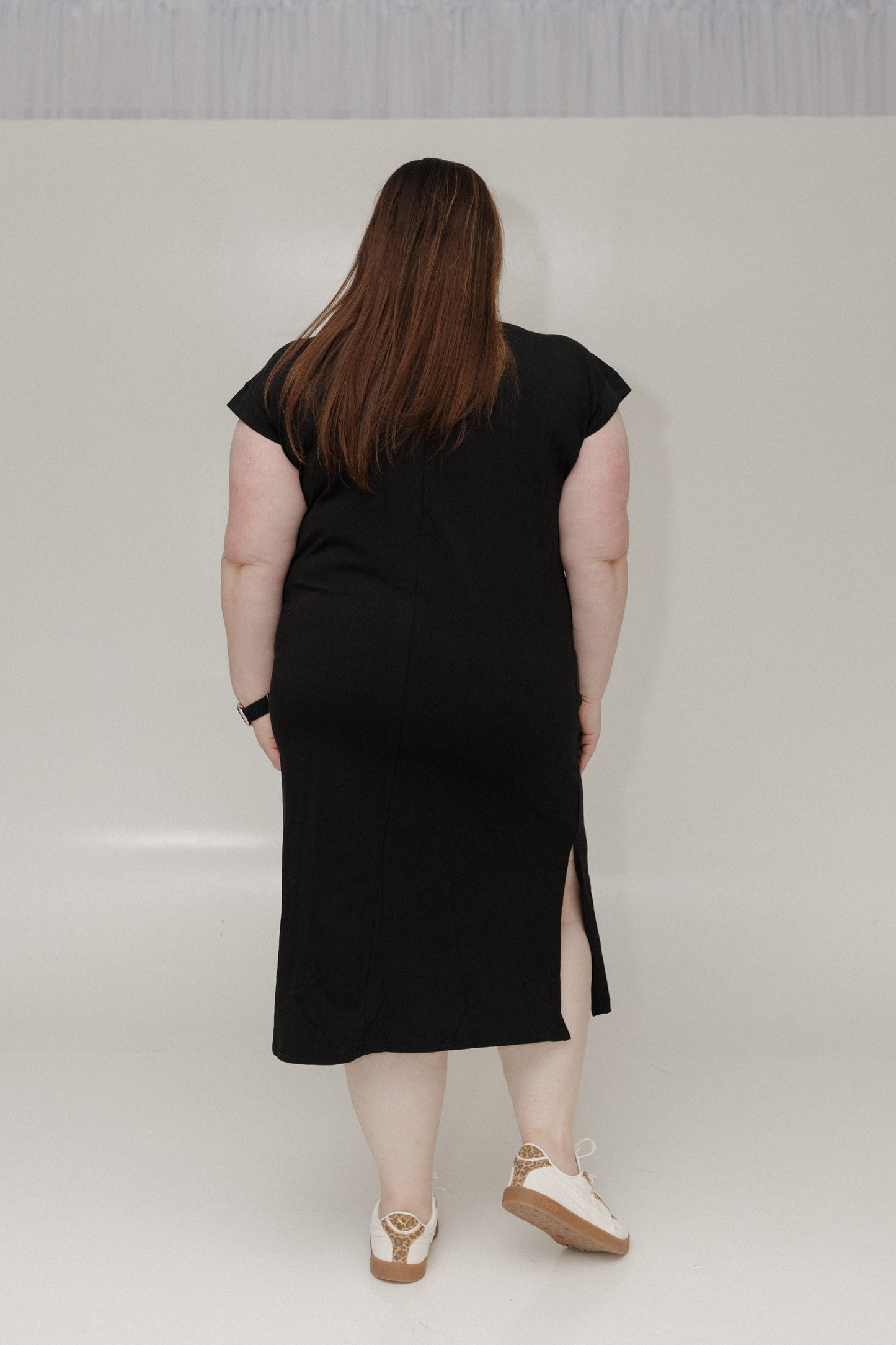 Person wearing a black dress with a slit on a plain background